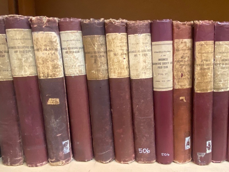Row of worn maroon hardback volumes titled ‘Transactions of the Inverness Scientific Society and Field Club,’ showing various early volumes lined on a shelf.