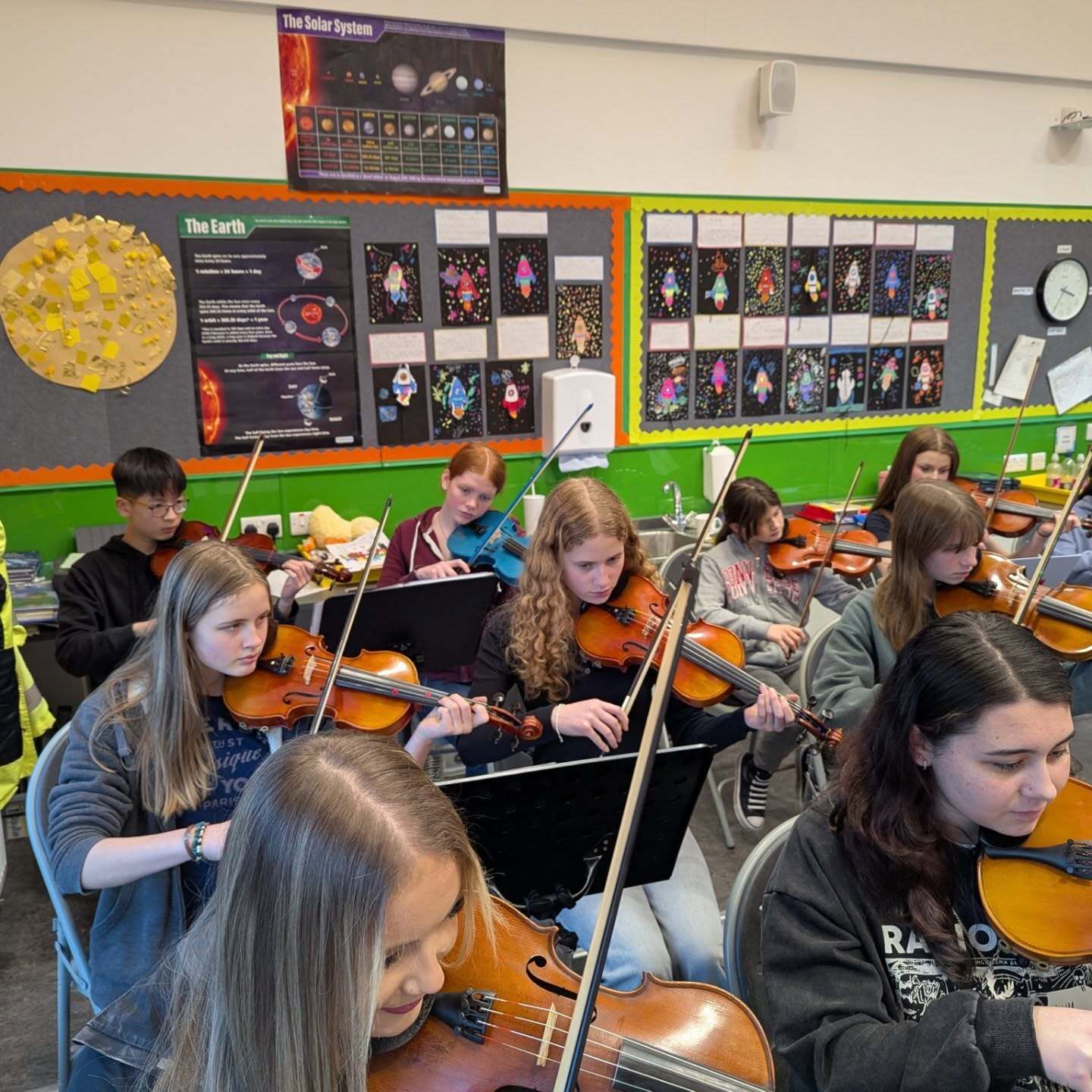 Group of pupils playing violins during a school music lesson in a classroom.