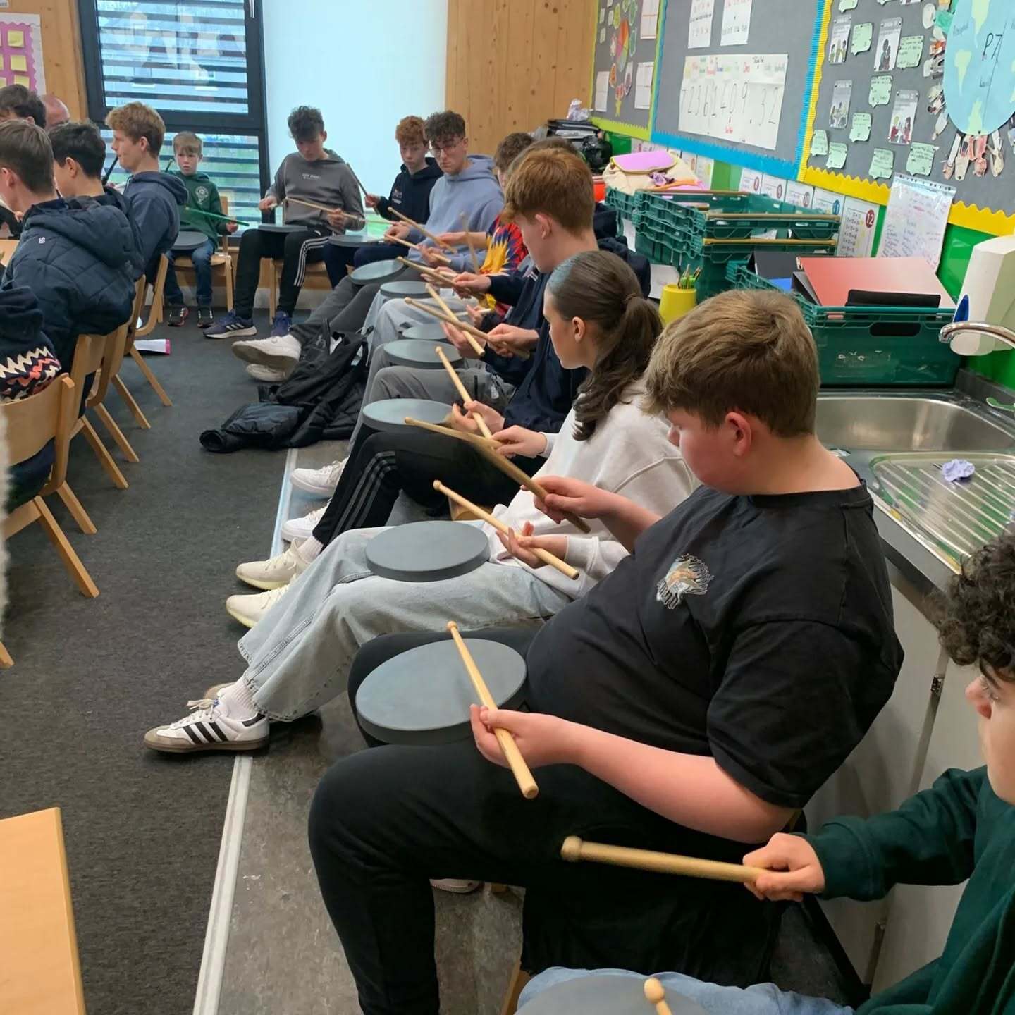 Pupils seated in a classroom practising drumming techniques with drum pads and sticks.