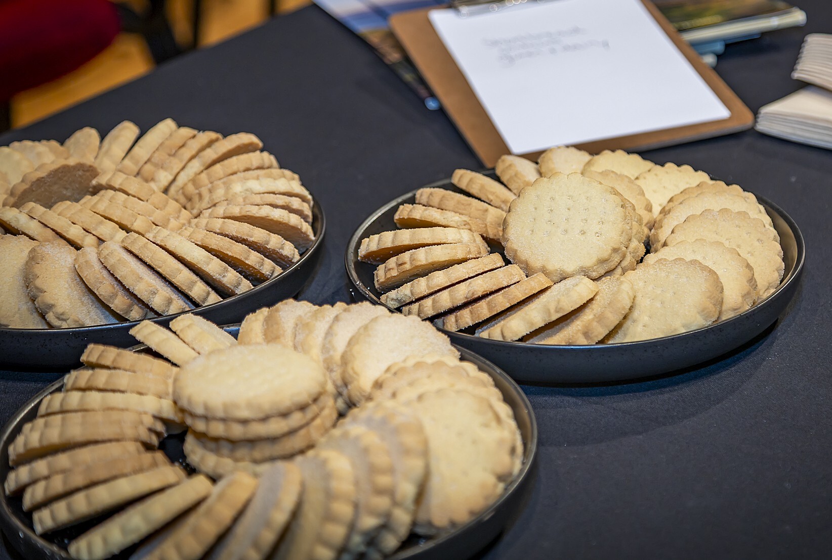 Three plates of round shorbread biscuits on a table covered with a dark tablecloth.