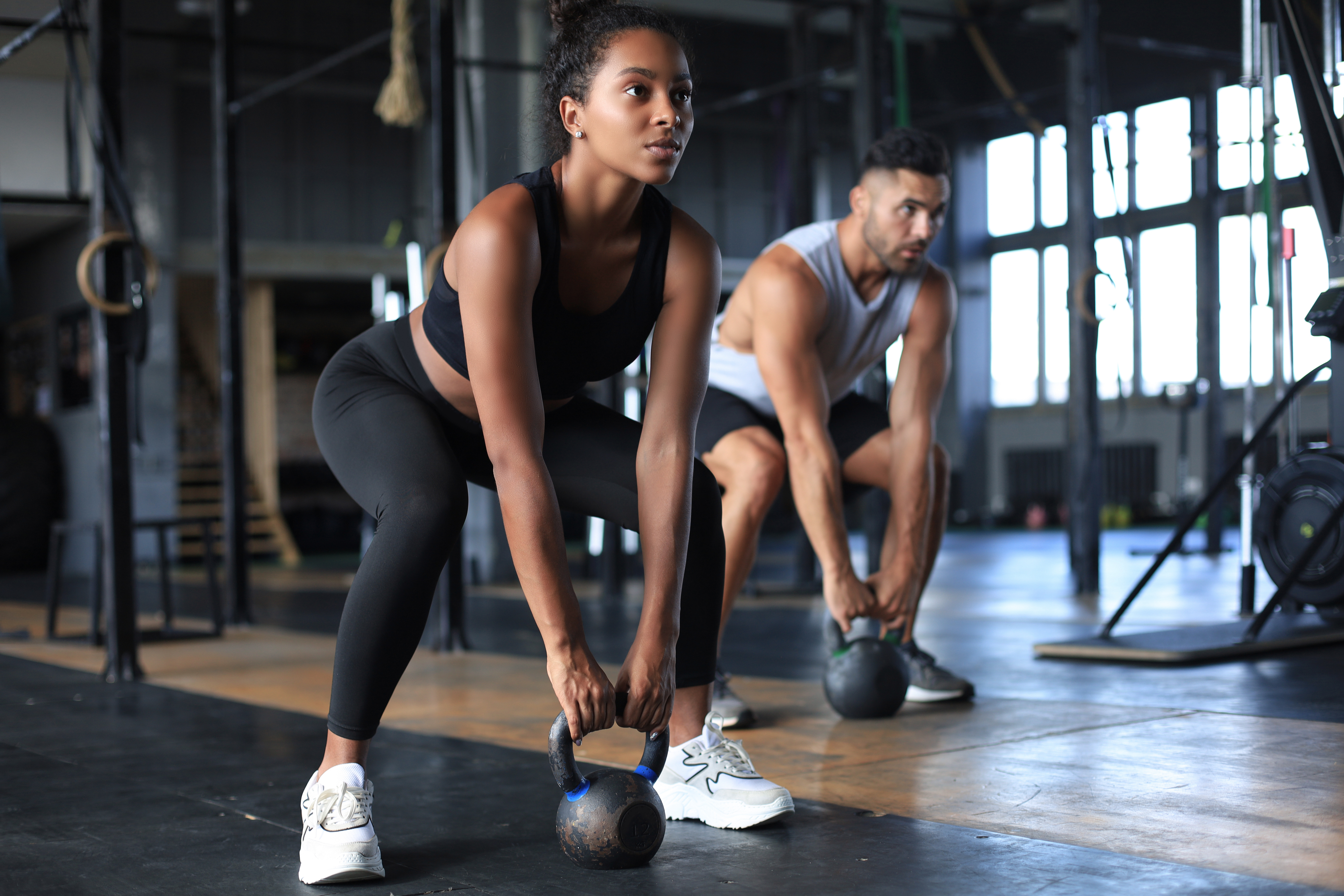 Two people in a gym setting lifting kettlebells