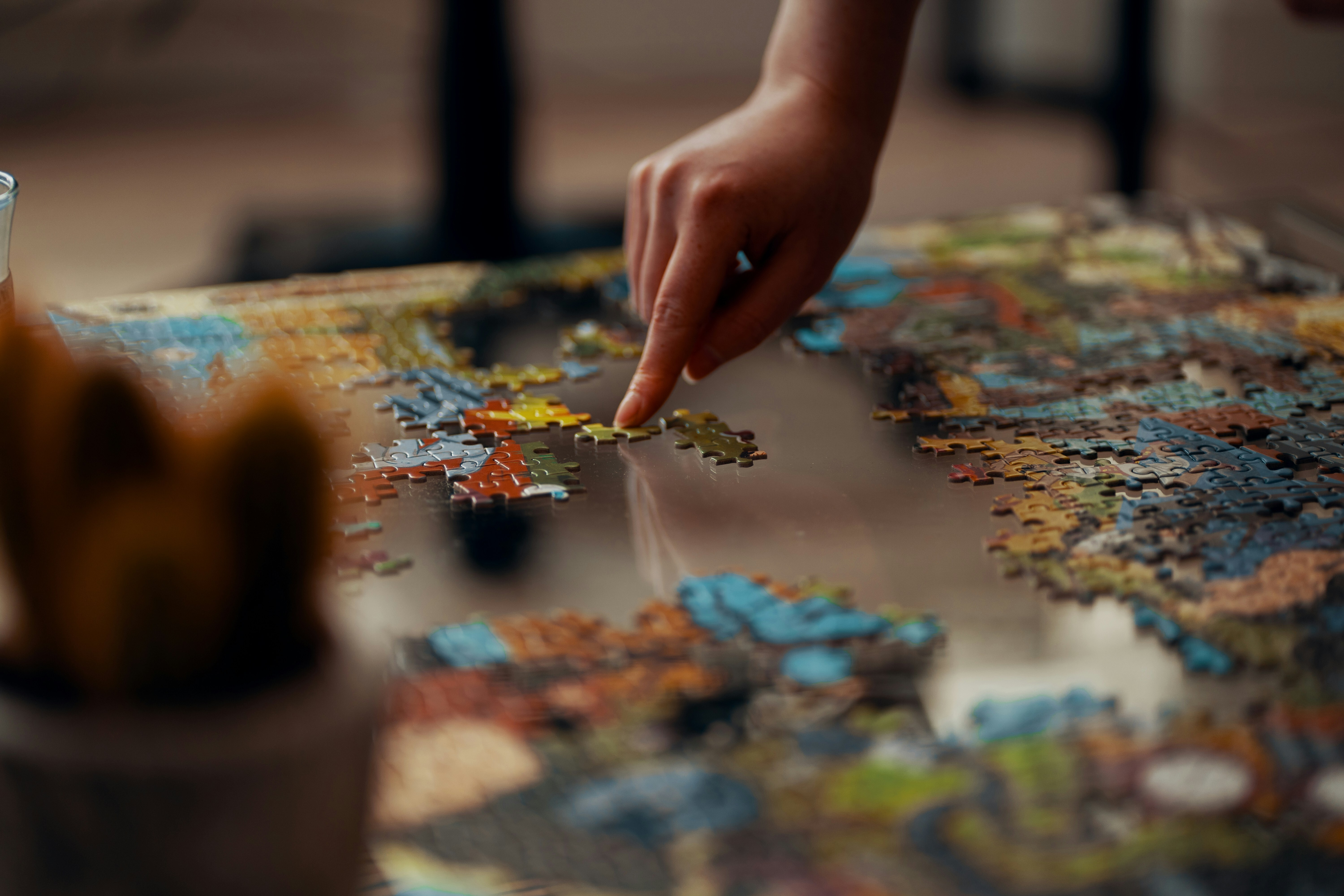 Close-up of a hand placing a jigsaw puzzle piece on a table