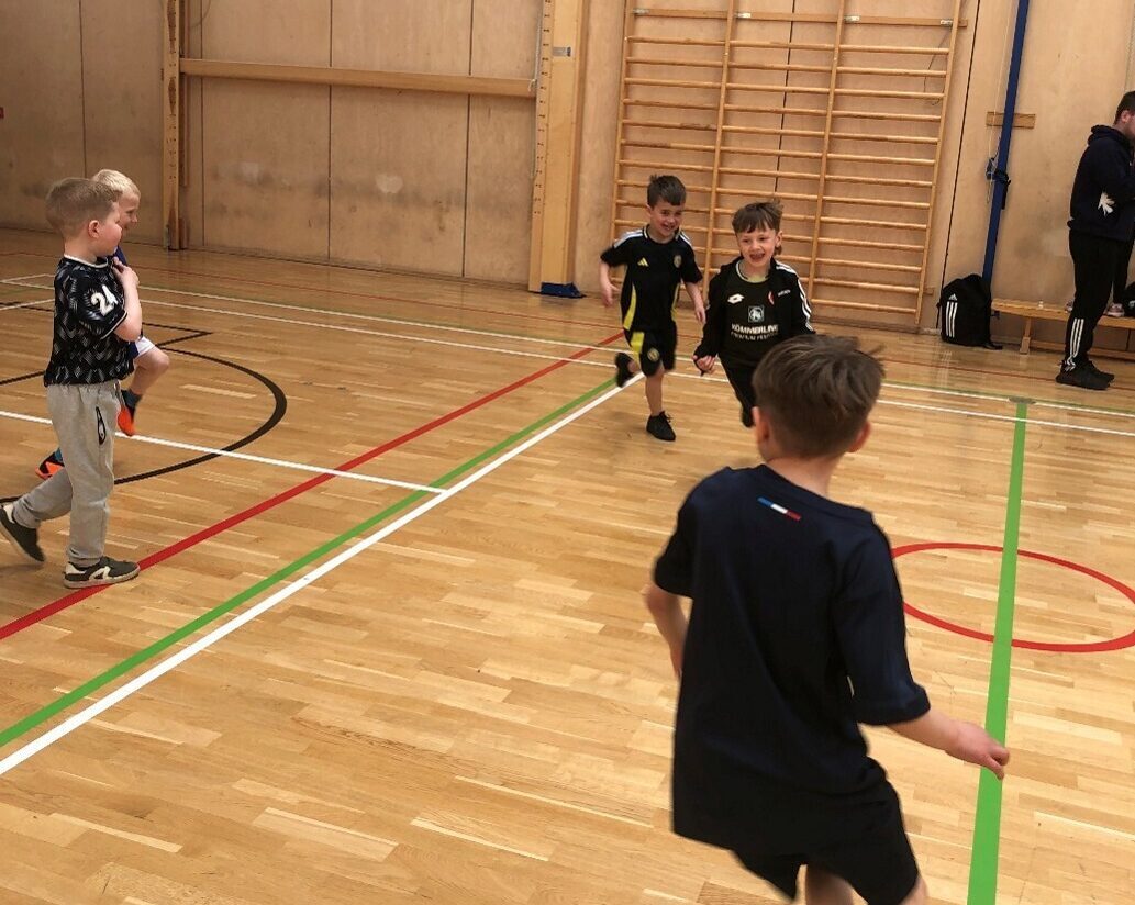 Four young boys running in a gym hall and smiling.