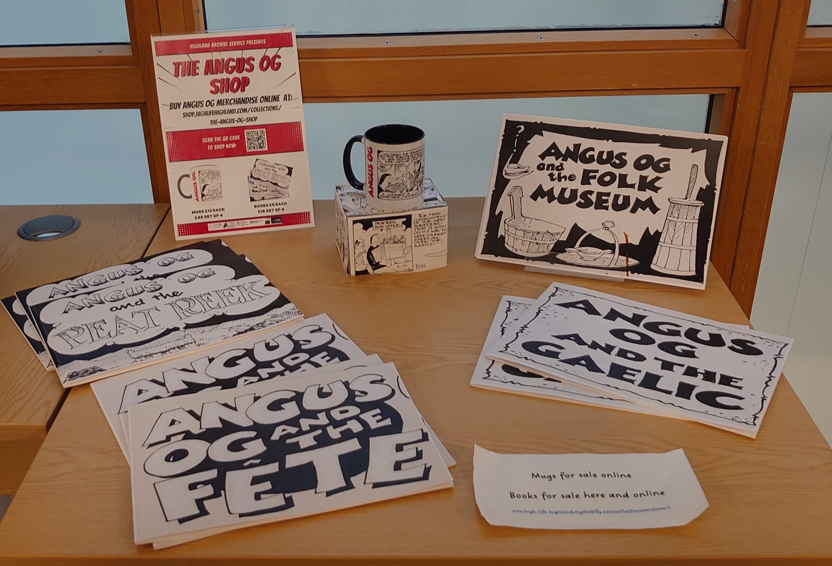 A table displaying Angus Og–themed posters, flyers, and a mug arranged neatly.