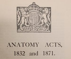 Printed page showing a detailed illustration of the British royal coat of arms with a crown, lion, and unicorn above a shield. Below the image, the text reads: “ANATOMY ACTS, 1832 and 1871.