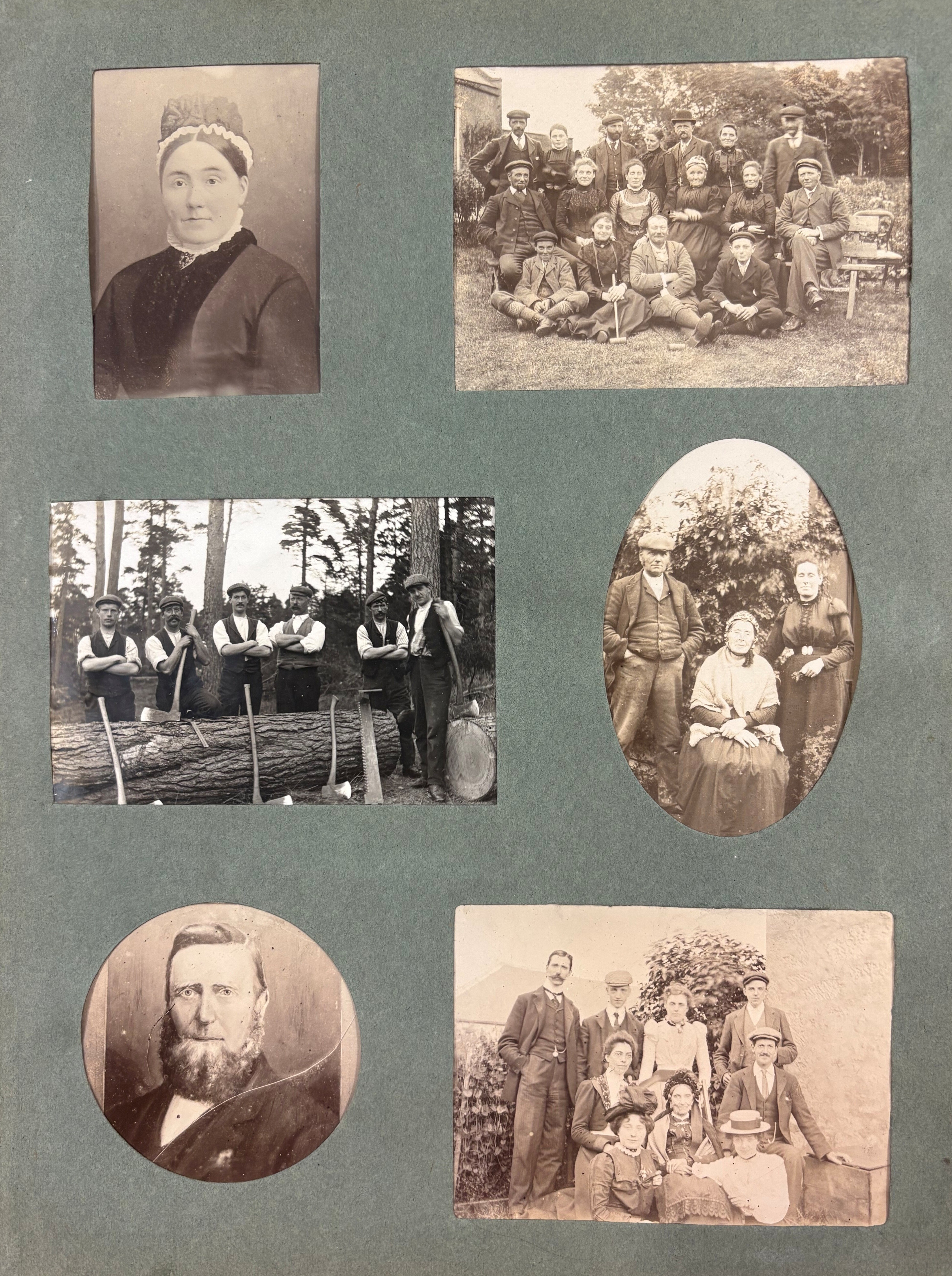 A scrapbook page featuring five black-and-white photographs arranged on a green background. The images include: a rectangular portrait of a person wearing a dark dress with a decorative collar; a group photo of about fifteen people seated and standing outdoors, some holding walking sticks; a photo of six individuals leaning on a large felled tree trunk with axes resting against it, suggesting logging work; an oval photo of three people outdoors, two standing and one seated, dressed in formal clothing; and a rectangular group portrait of ten people posed in front of a hedge, with some seated and others standing.