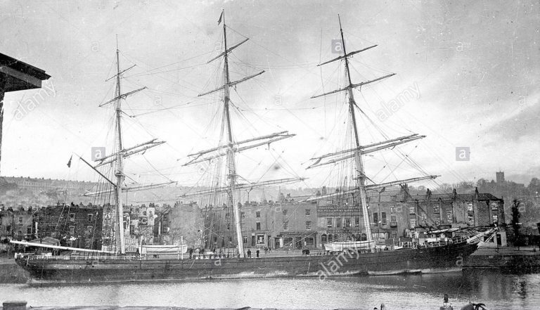 Black and white photograph of the Star of Germany sailing vessel showing three wooden masts and deck, with harbour and buildings in the background