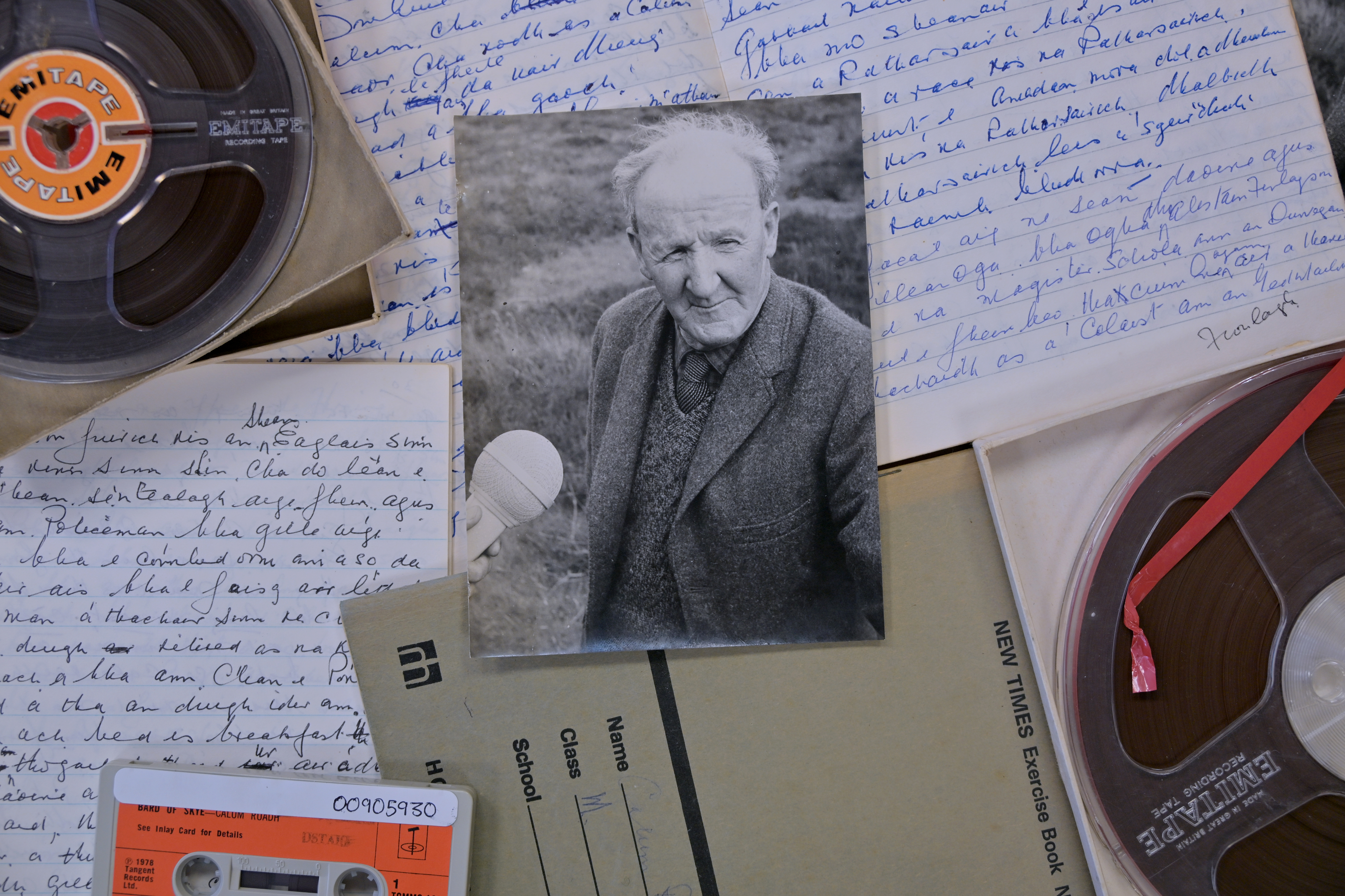 Collage image with back ground of open notebooks with Gaelic handwriting, reel to reel tapes and white and orange cassette tape. On top is black and white photo graph of Calum Ruadh Nicolson holding a ball