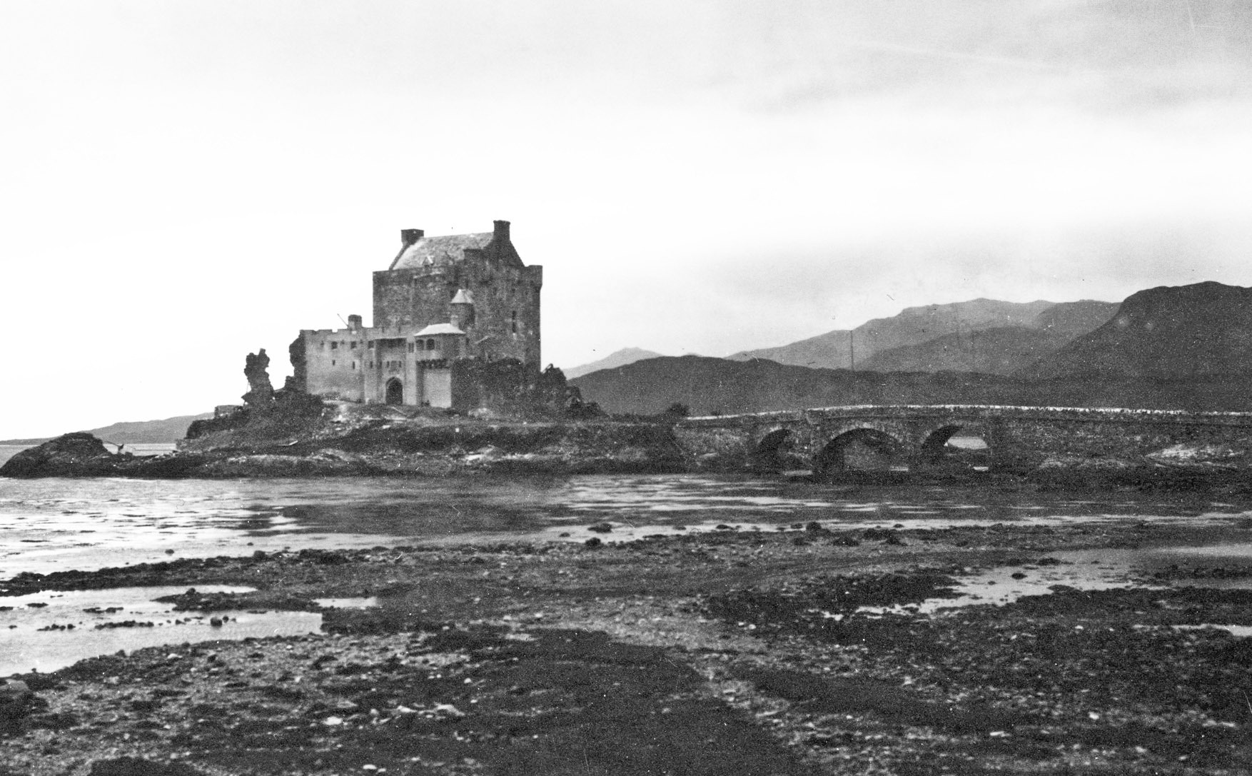 A black and white photograph of an arched bridge leading to a castle on a promontory