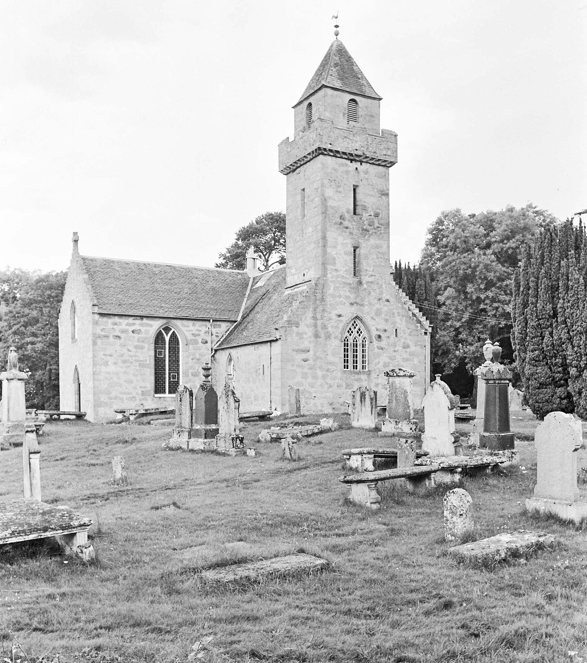 A black and white photograph of an old church building with the tower.  The foreground shows a graveyard.