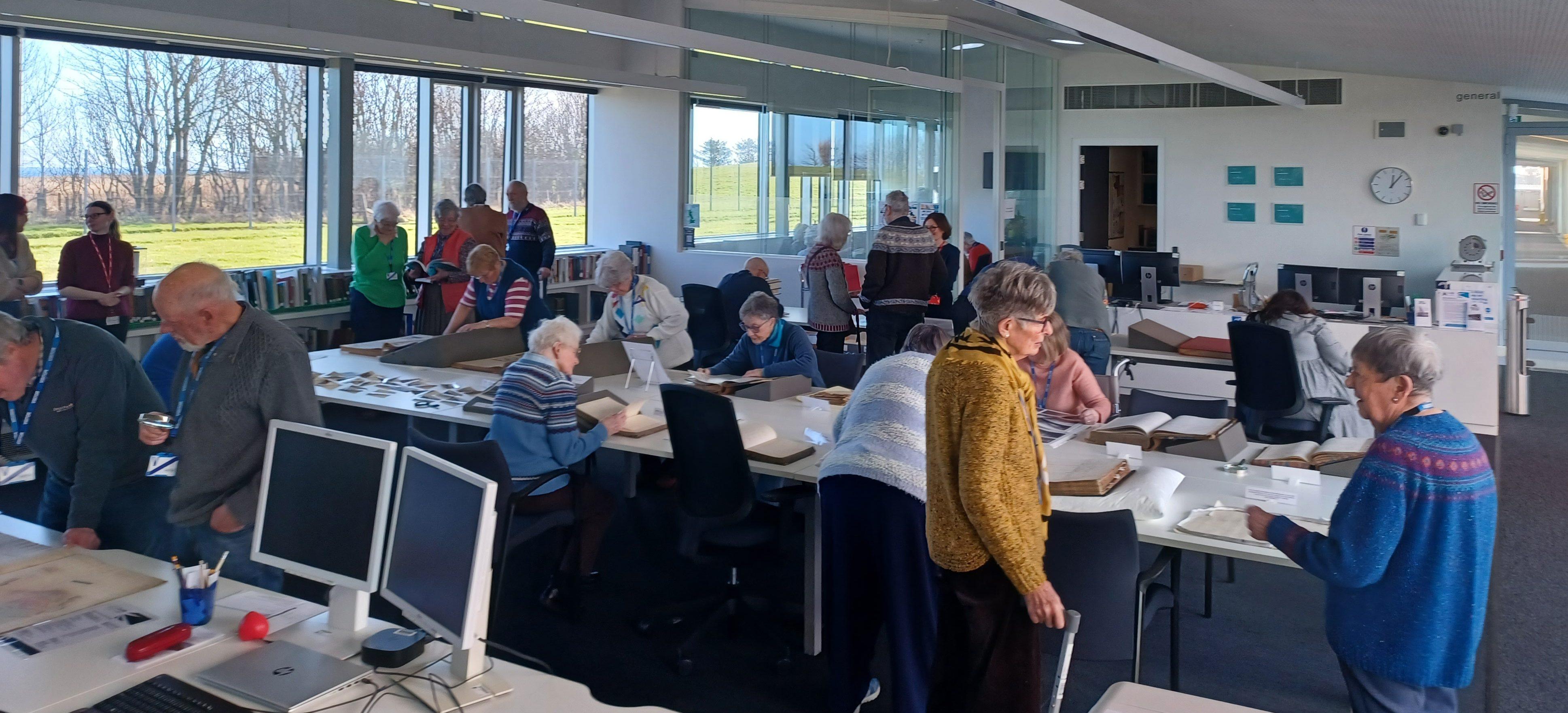 A light bright room with people looking at white tables covered with displays of historic documents.