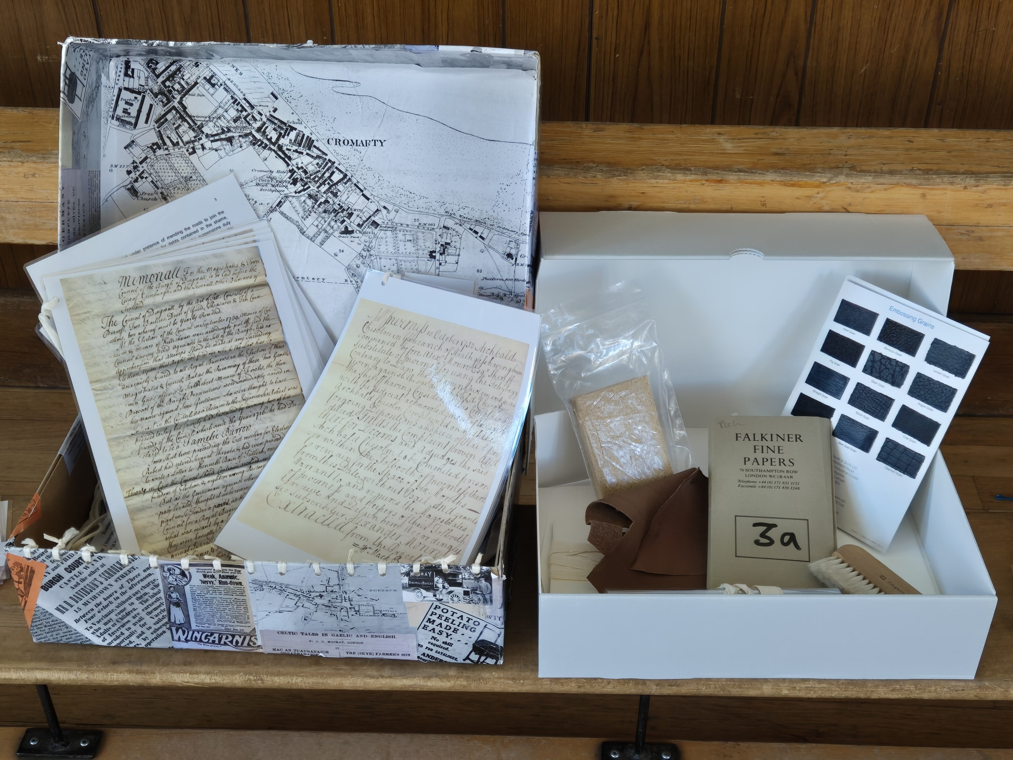 Two open boxes side by side.  One with copies of historic documents and one with samples of papers and leather.