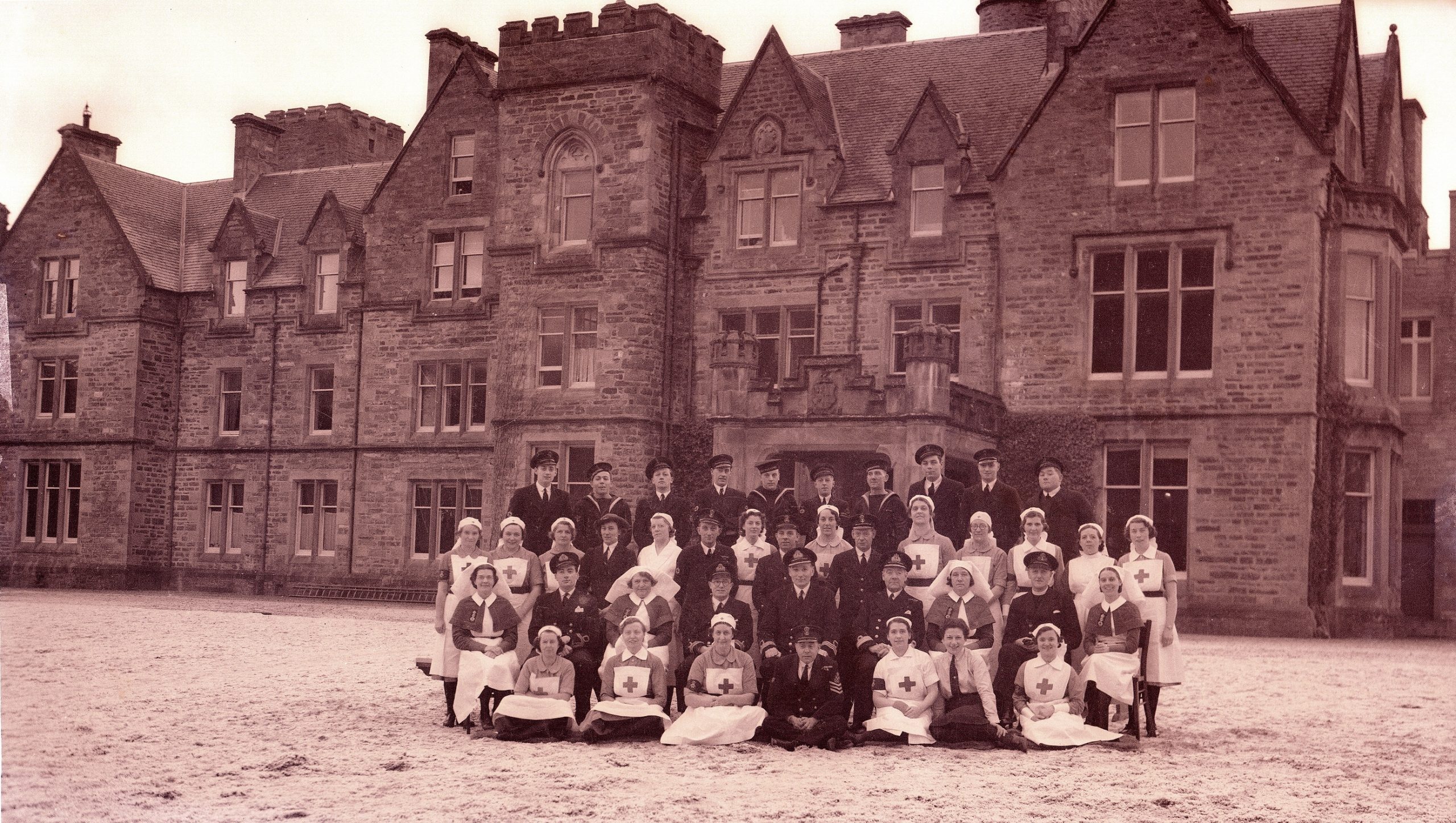 Sepia coloured photograph showing men and women in royal navy and nursing uniforms outside a large castle building