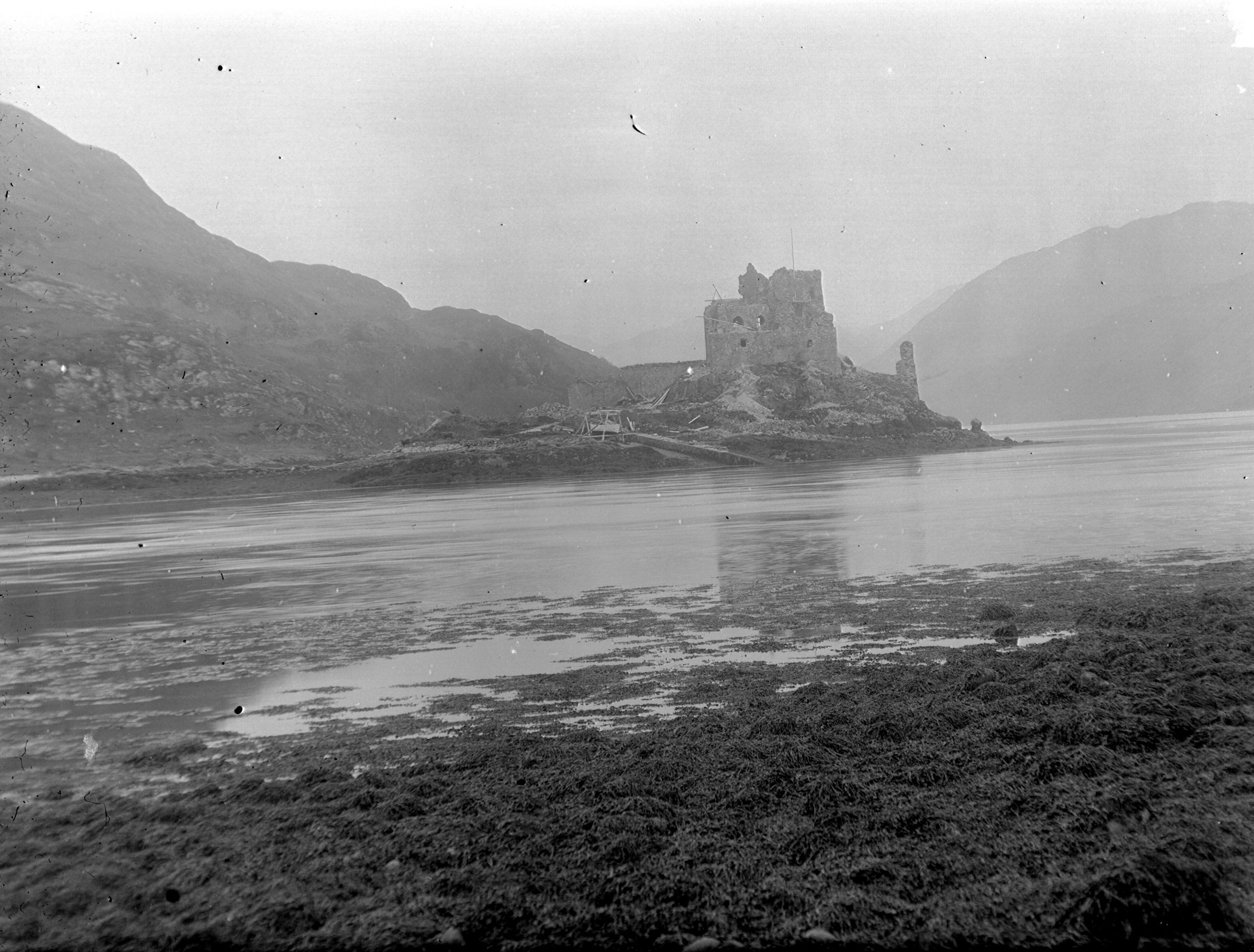 A black and white photograph showing a ruined castle on a promontory in silhouette against a light sky