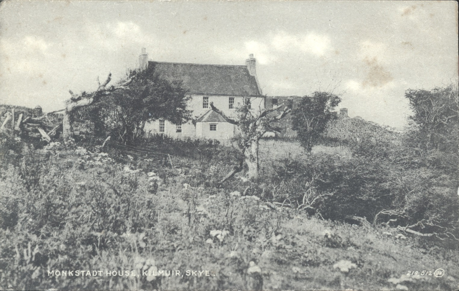 Black and white postcard showing a white house on a hillside with trees.  Text indicates that it is Monkstadt House in Kilmuir, Isle of Skye