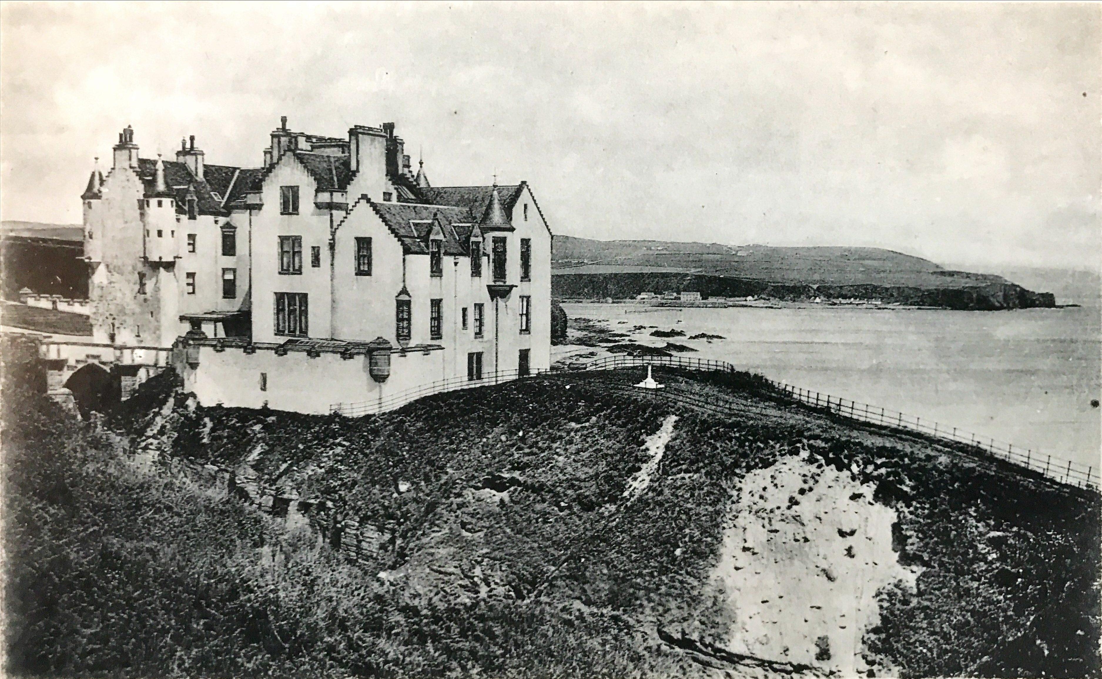 A black and white image of a white castle on a cliff edge with the sea behind