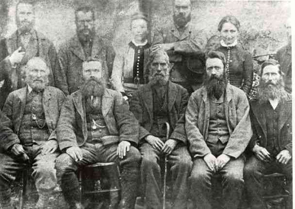 A faded black and white photograph showing a group of 9 men and 2 women, seated and standing