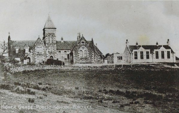 Black-and-white photograph of a large stone school building with a central tower and arched windows, flanked by smaller adjoining structures. The building sits on a grassy slope with sparse vegetation. Text at the bottom reads “Higher Grade Public School, Portree.”