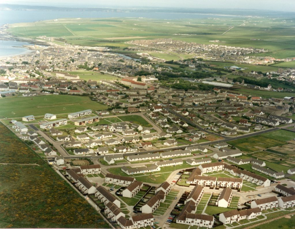 Aerial view of Thurso showing housing estates, green fields, coastline, and sea in the distance.