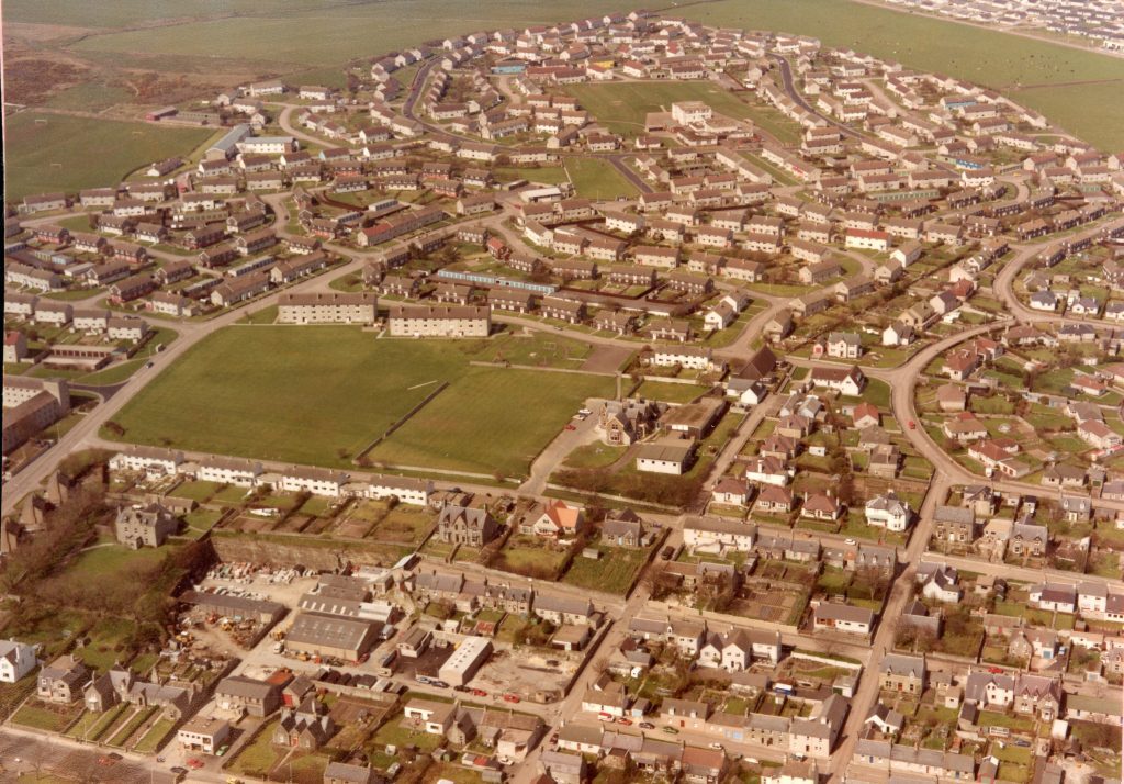 Aerial view of Thurso showing housing estates, curved streets, green spaces, and surrounding open fields.