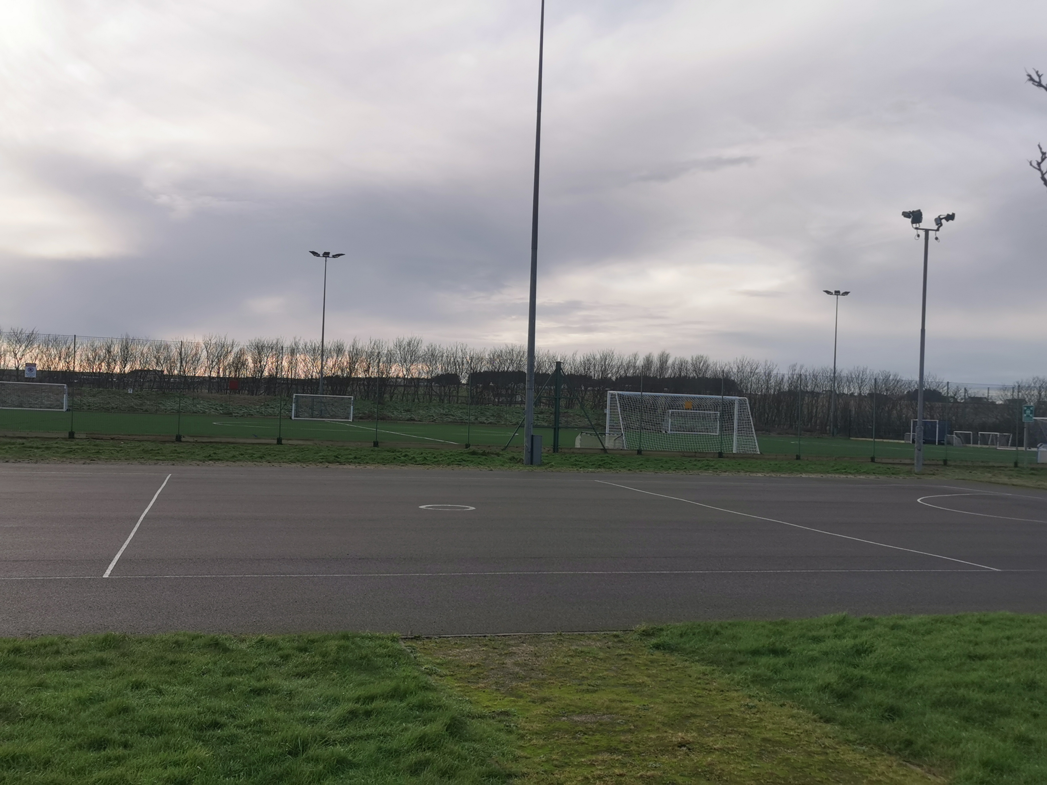 An outdoor all-weather pitch with floodlights around the perimeter and goals at each end.