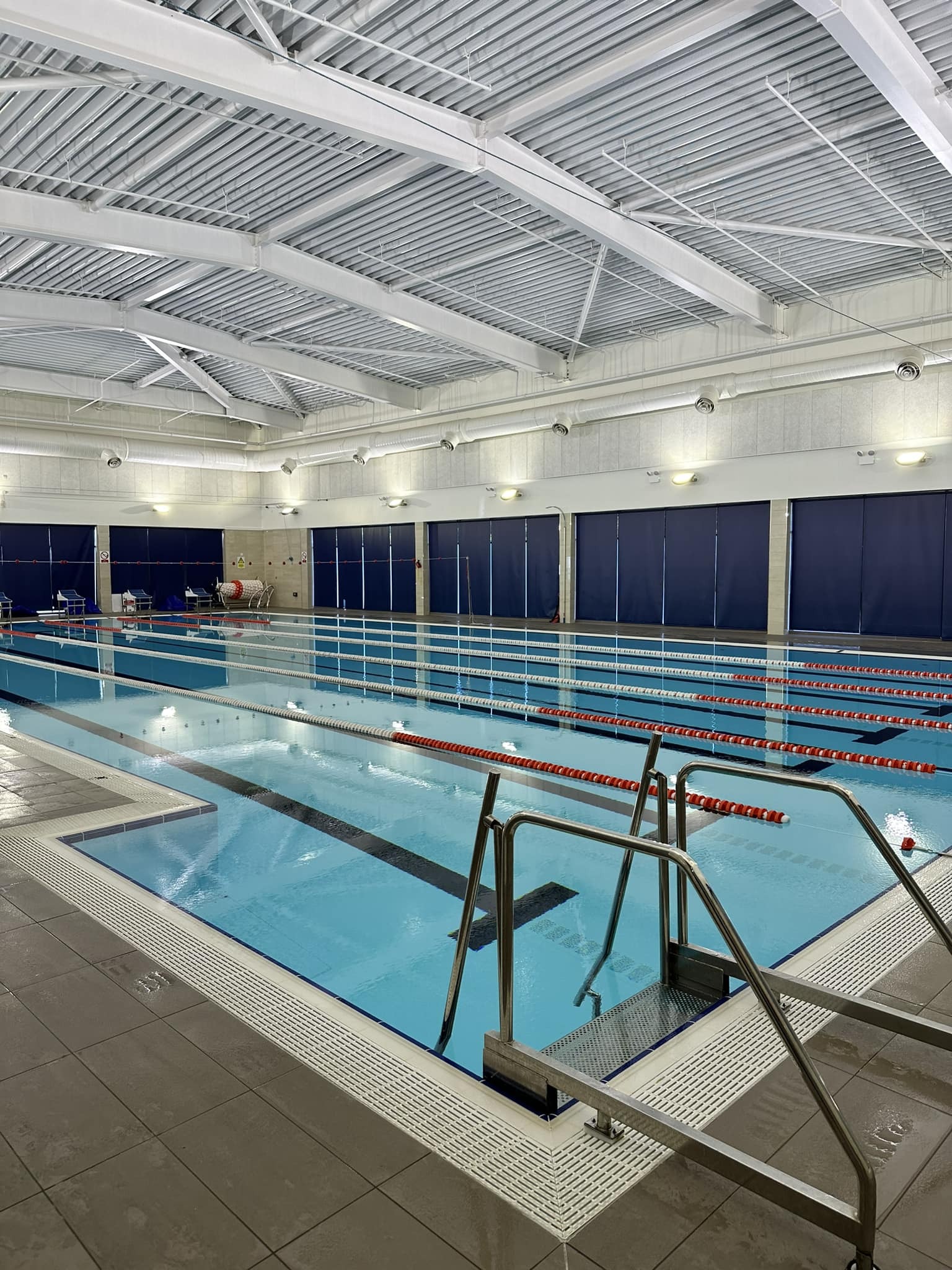 A wide view of an indoor swimming pool with multiple swimming lanes and clear blue water.