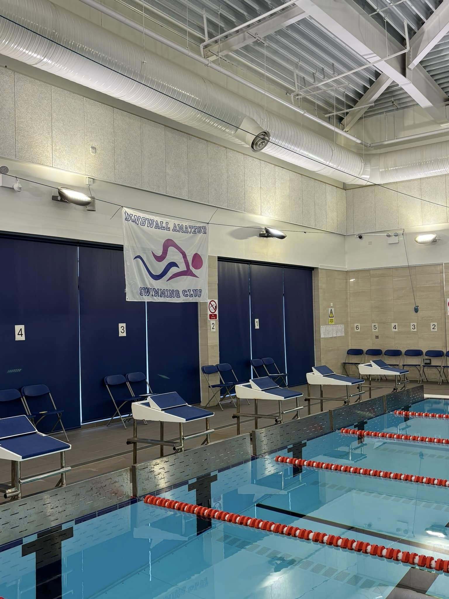A view along the side of an indoor swimming pool showing starting blocks.