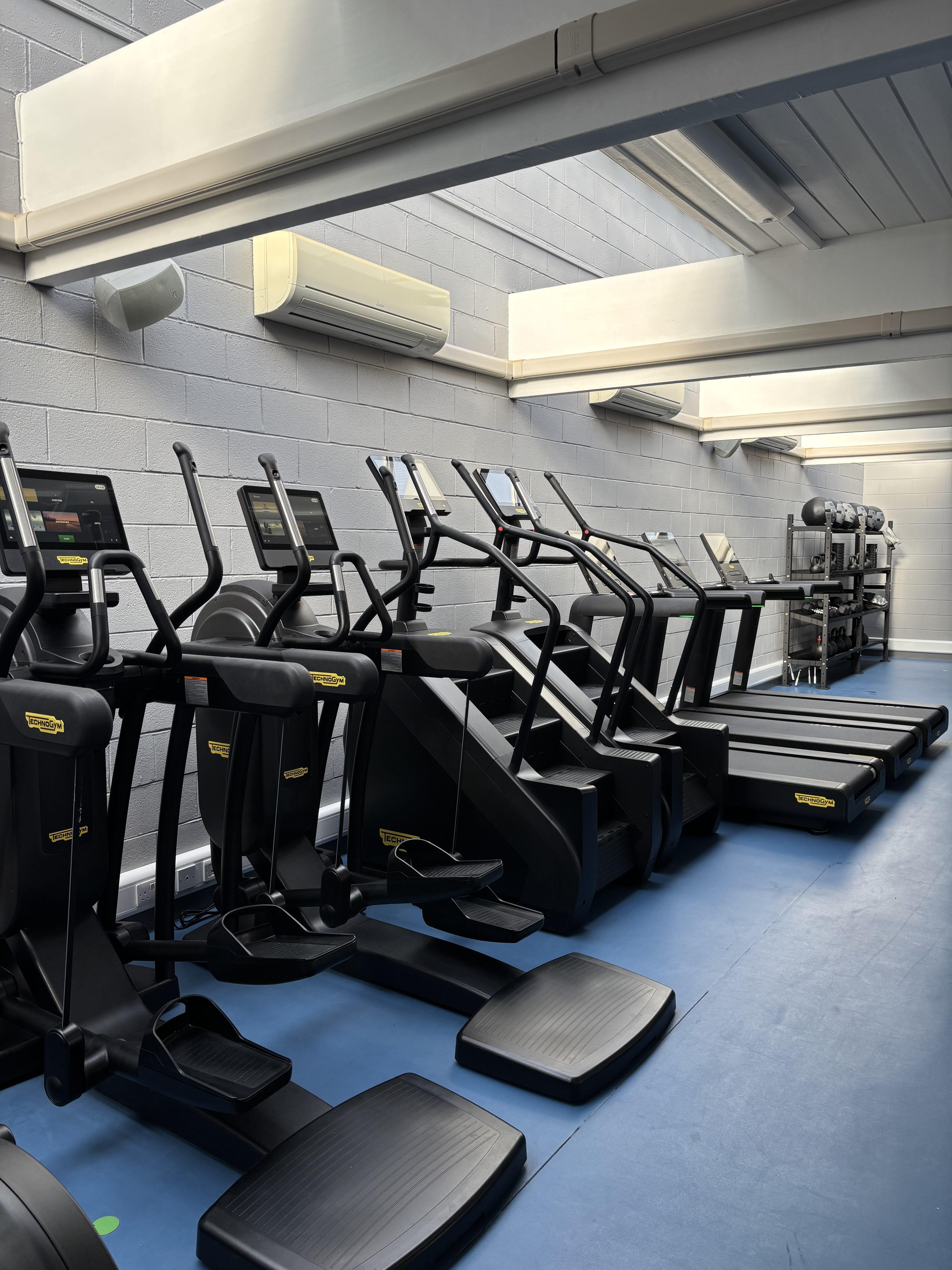 Row of stair-climber machines in a gym with blue flooring and grey walls.