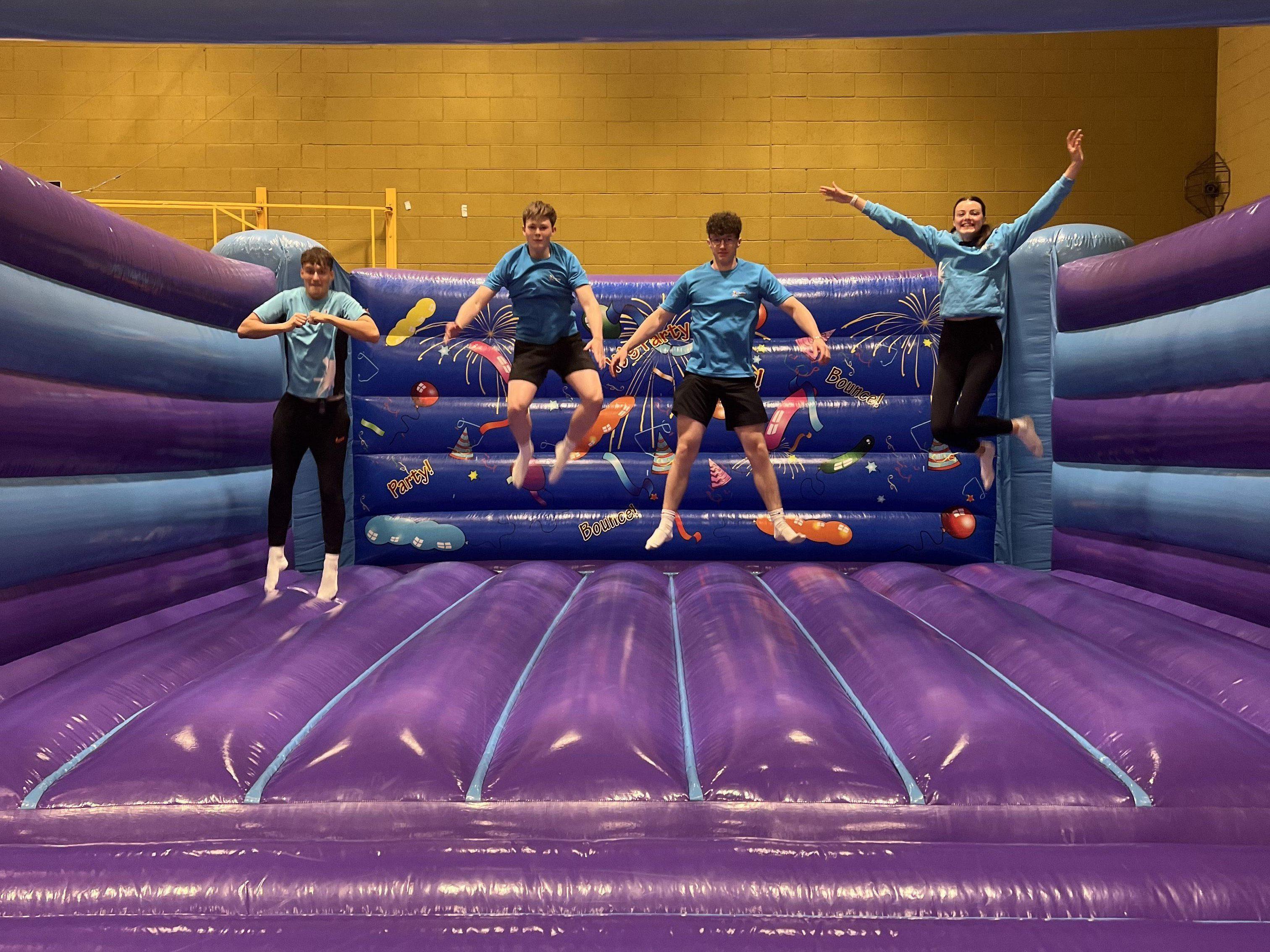 Group of people jumping on a purple inflatable bouncy castle indoors.