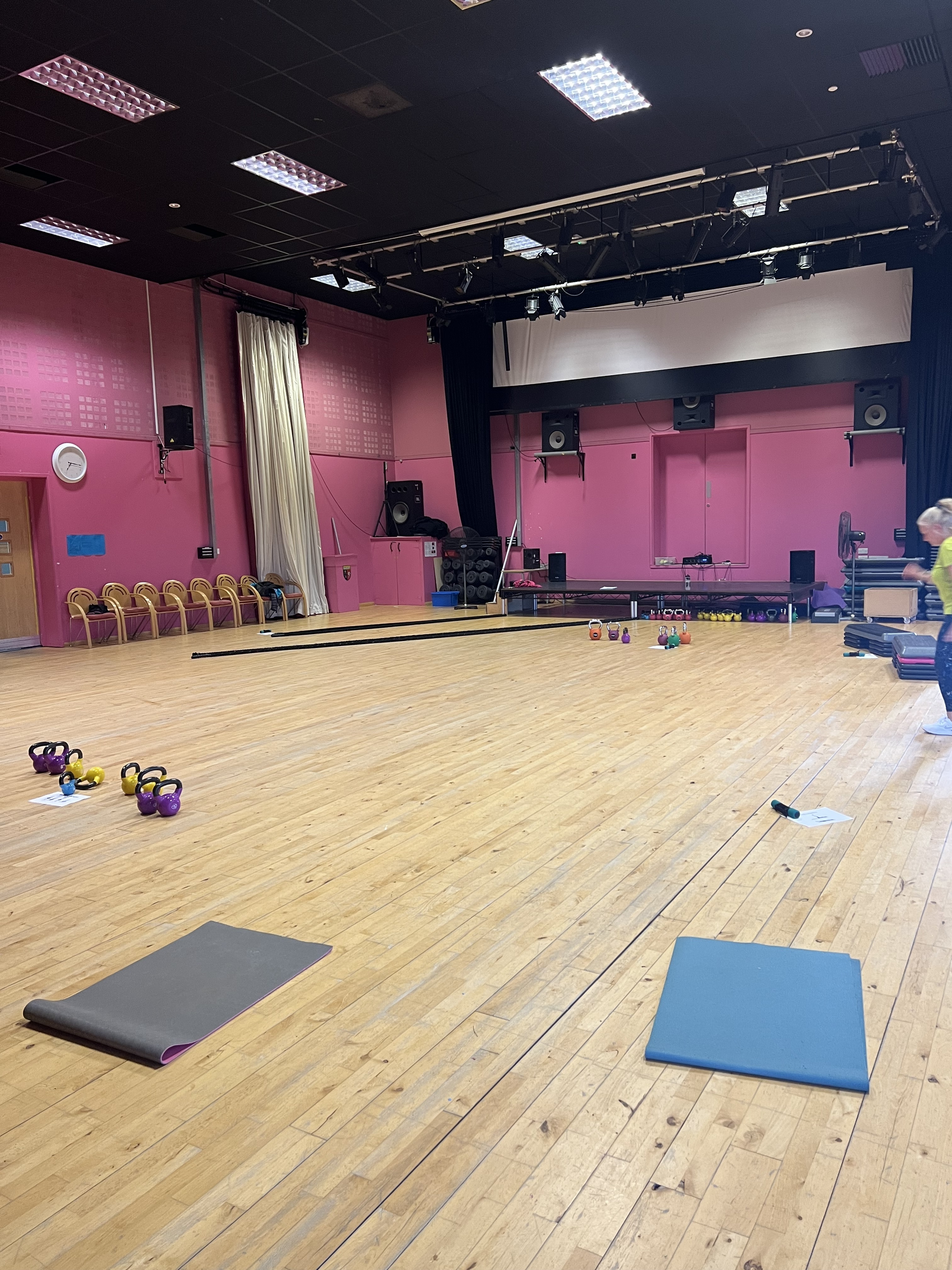 A large hall with exercise mats and kettlebells on the floor for a group fitness class.