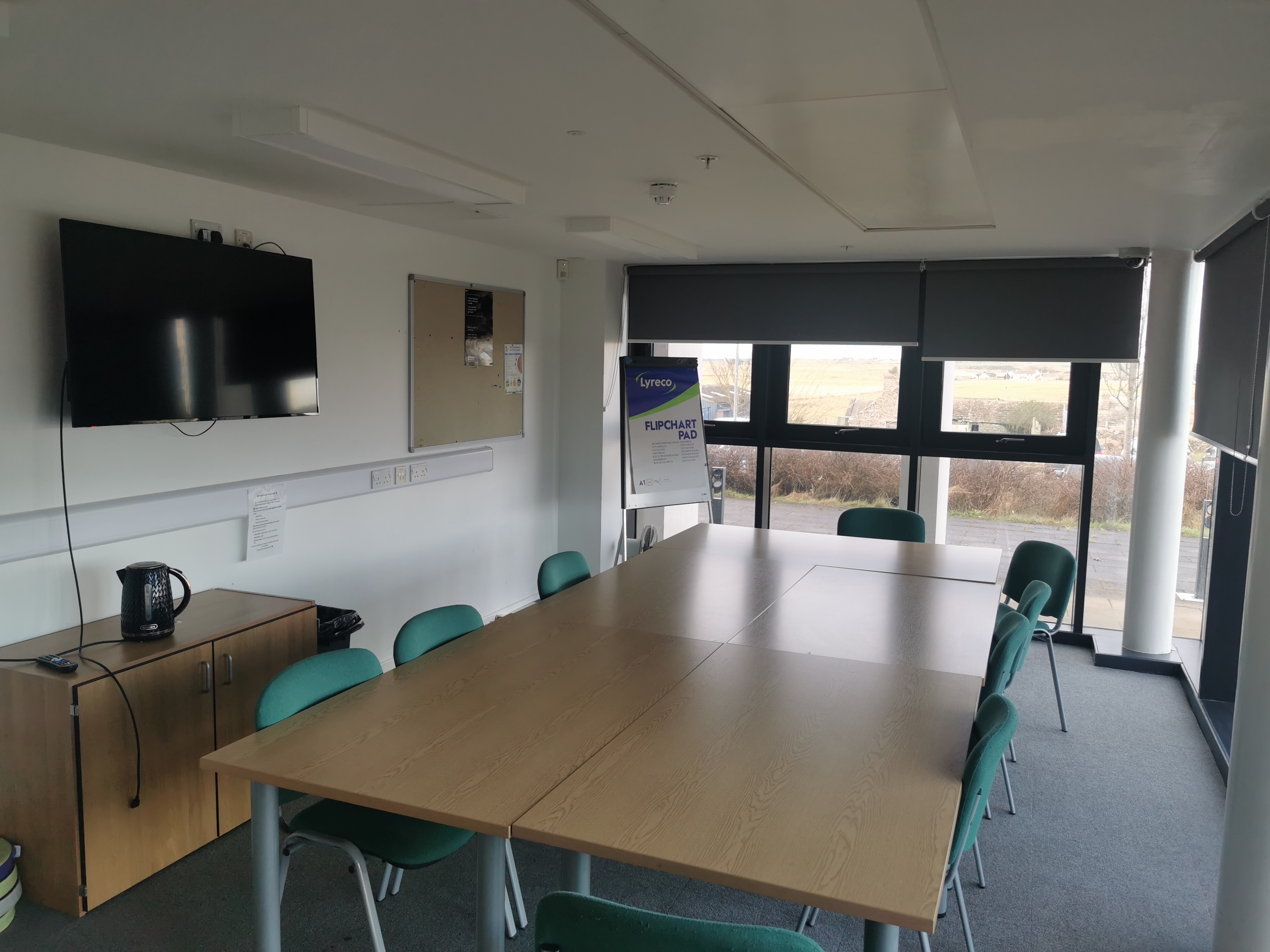 A meeting room set up including tables, chairs and TV screen.