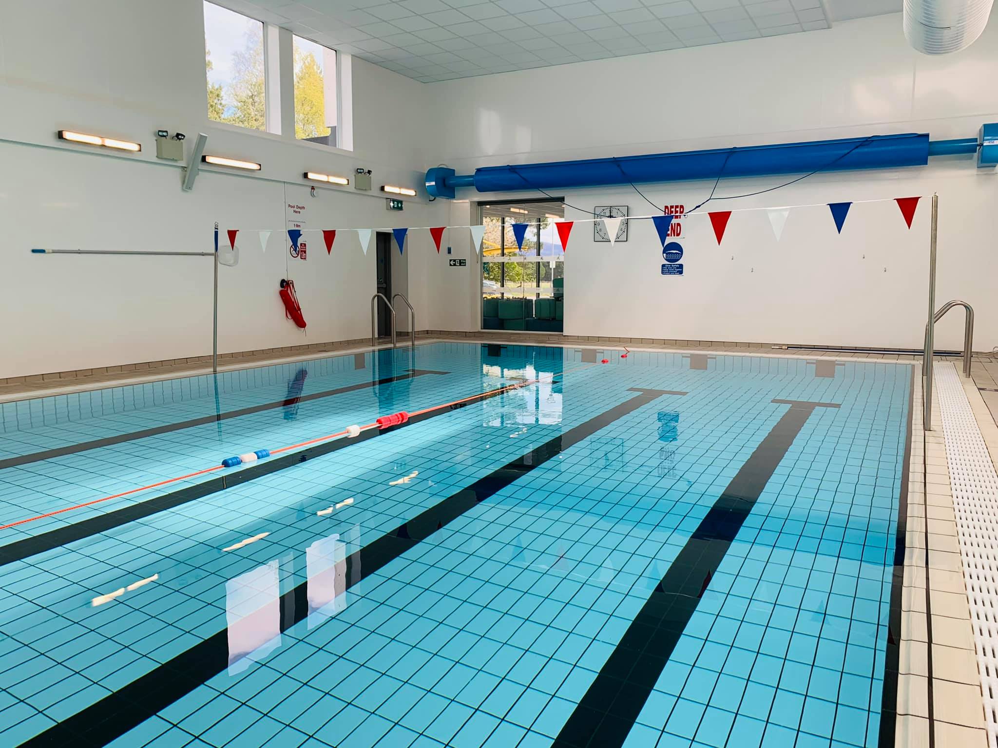 Indoor swimming pool with clear blue water, lane markers, and natural light from large windows.