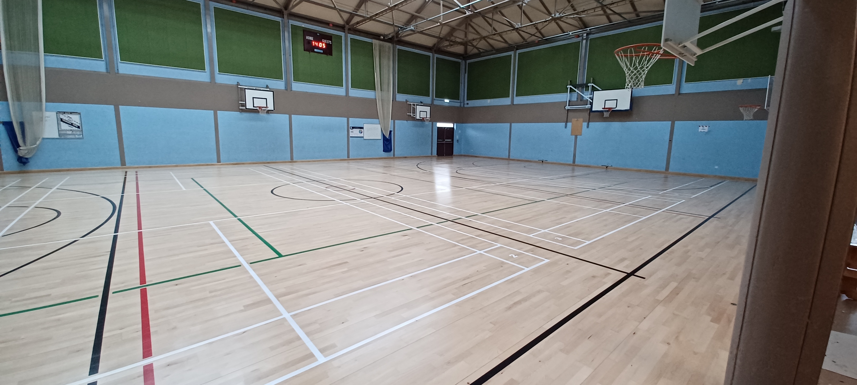 Large games hall with basketball and badminton court markings on the floor and basketball hoops on the walls.