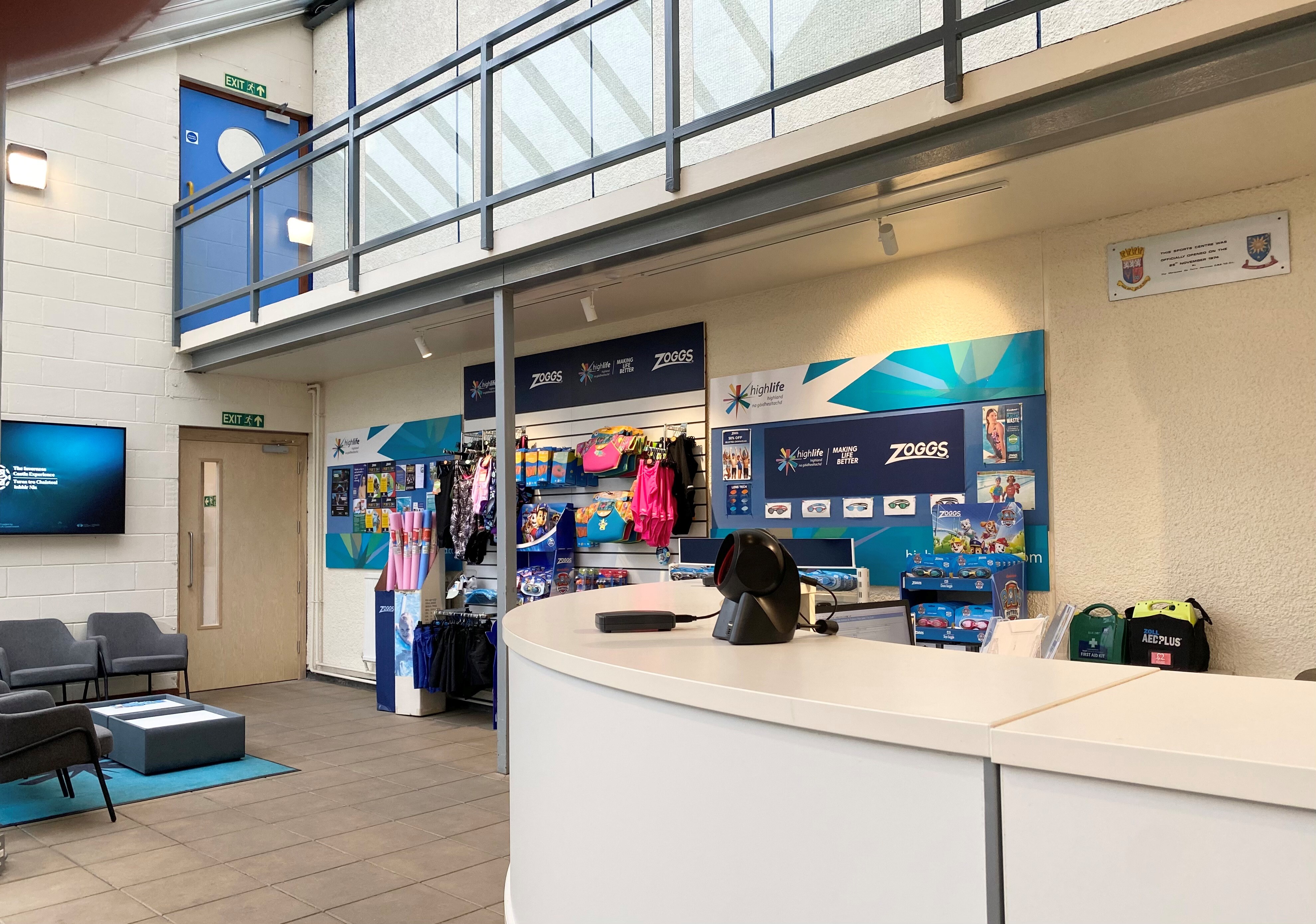 Curved reception desk with a balconny overhead and chairs agaist the side wall.