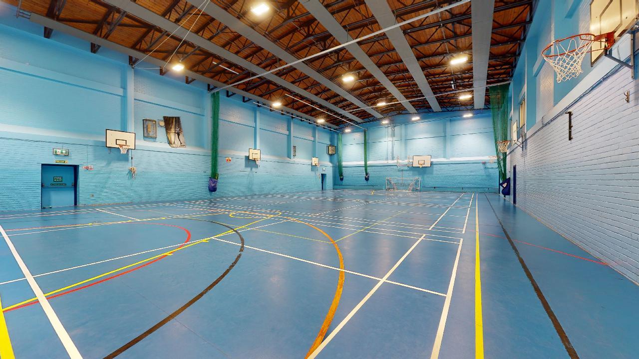Spacious indoor sports hall with basketball hoops and court markings on a polished floor.