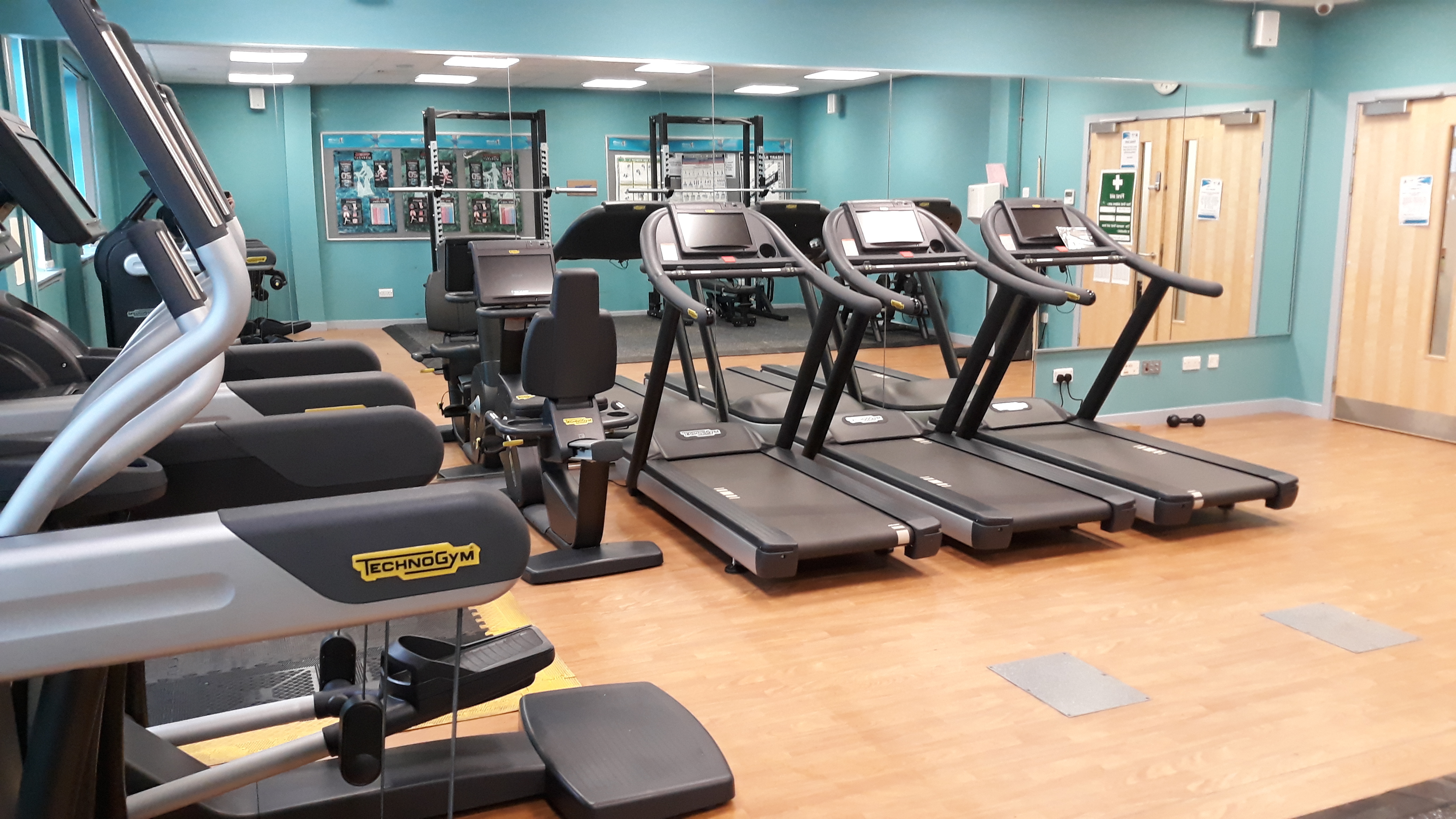 A gym area with treadmills and other cardio machines facing mirrored walls.