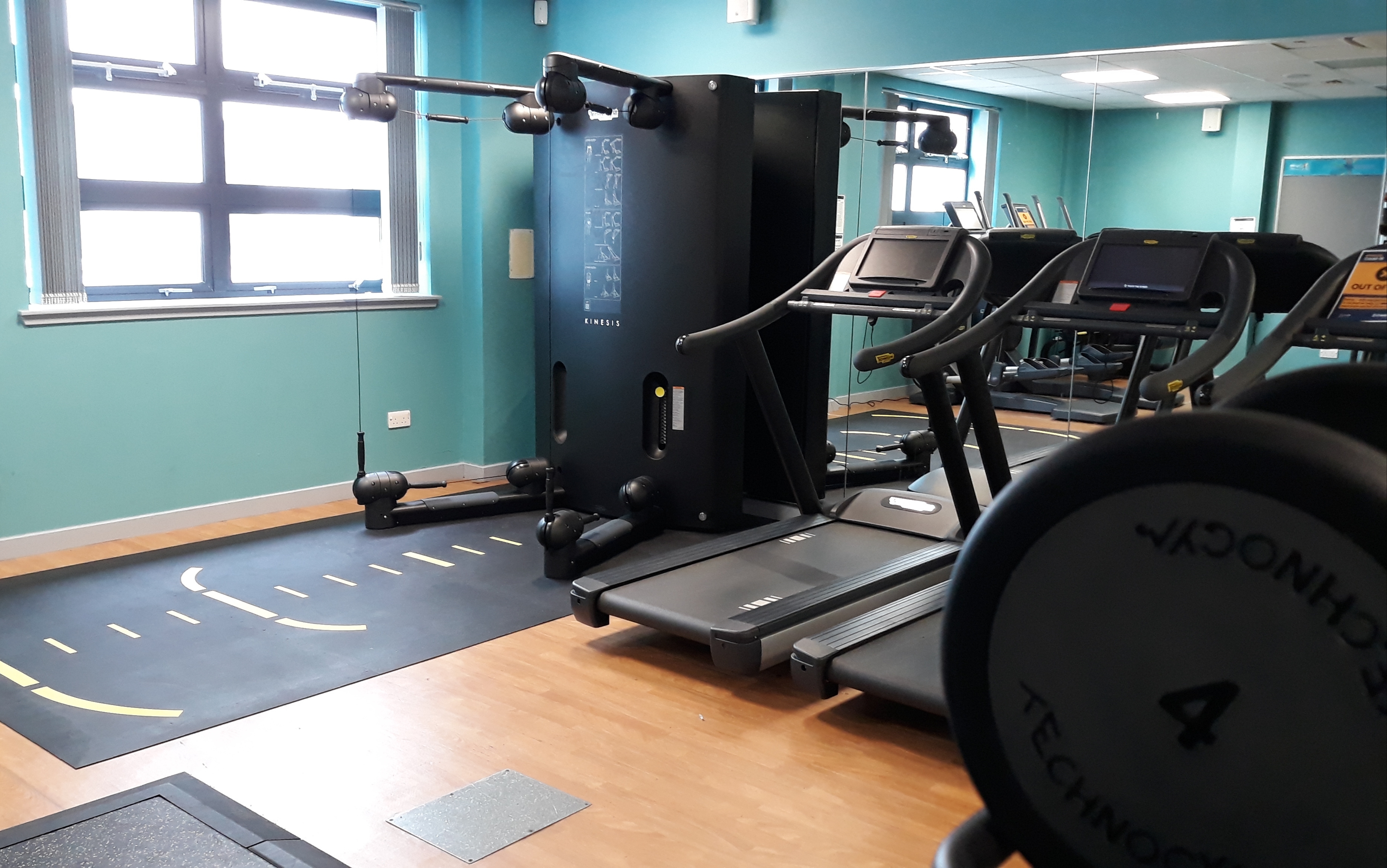 Gym area with a cable machine next to treadmills and a window letting in natural light.