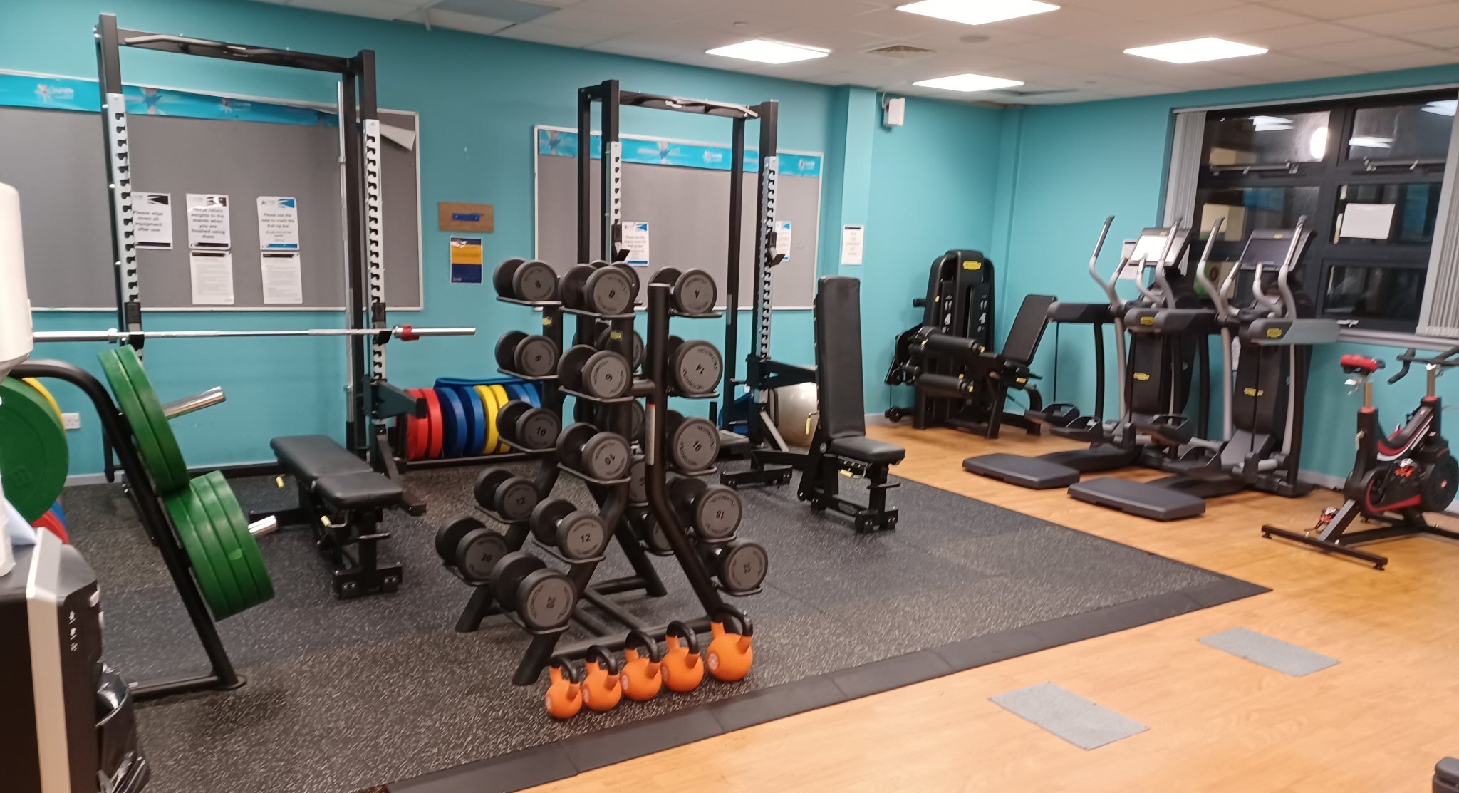 A gym space with weightlifting racks, dumbbells, benches and kettlebells on rubber flooring.
