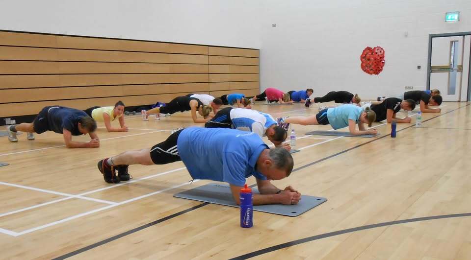 A group of people holding a plank position on exercise mats in a sports hall.
