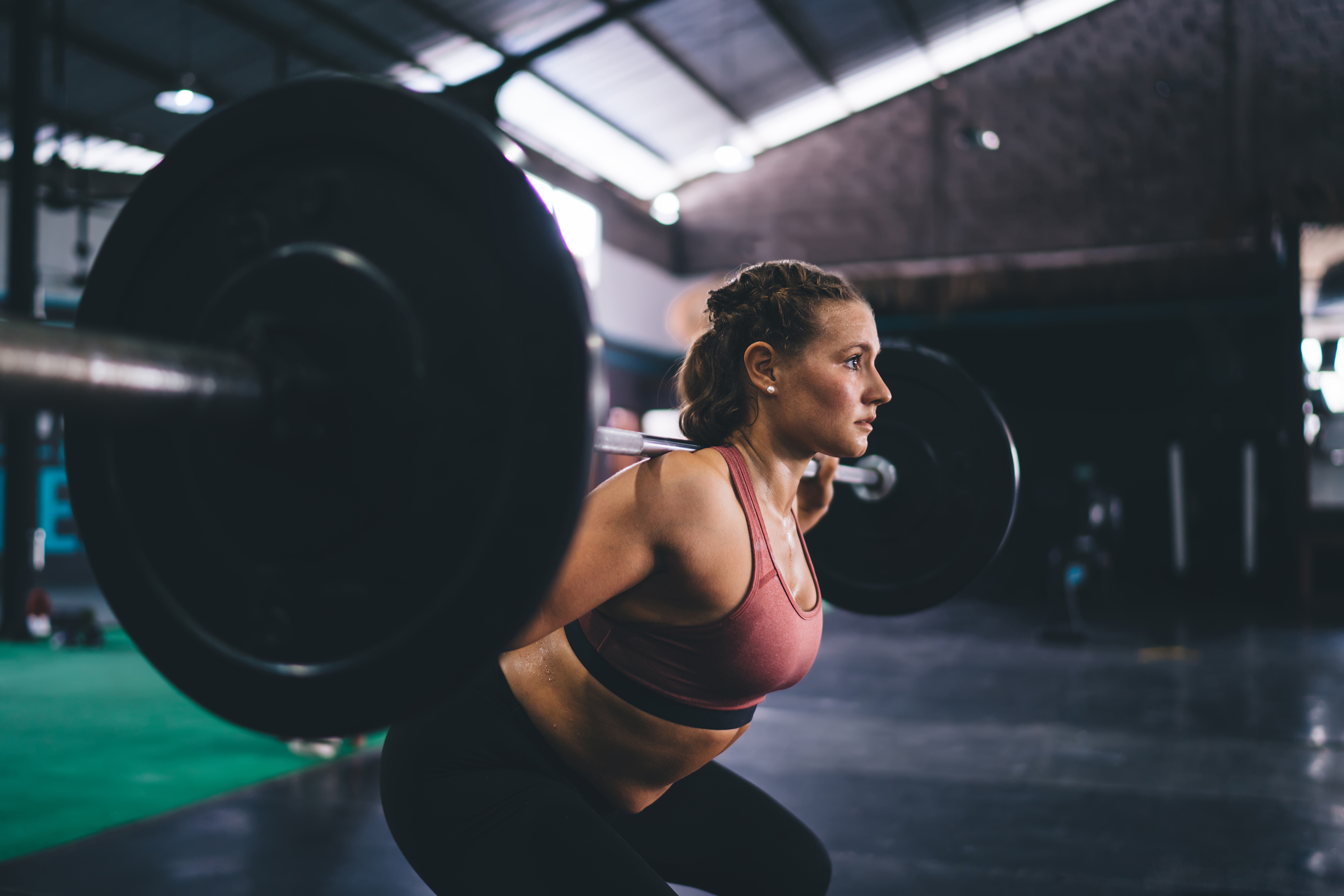 A person performing a back squat in a gym, holding a loaded barbell across their shoulders.