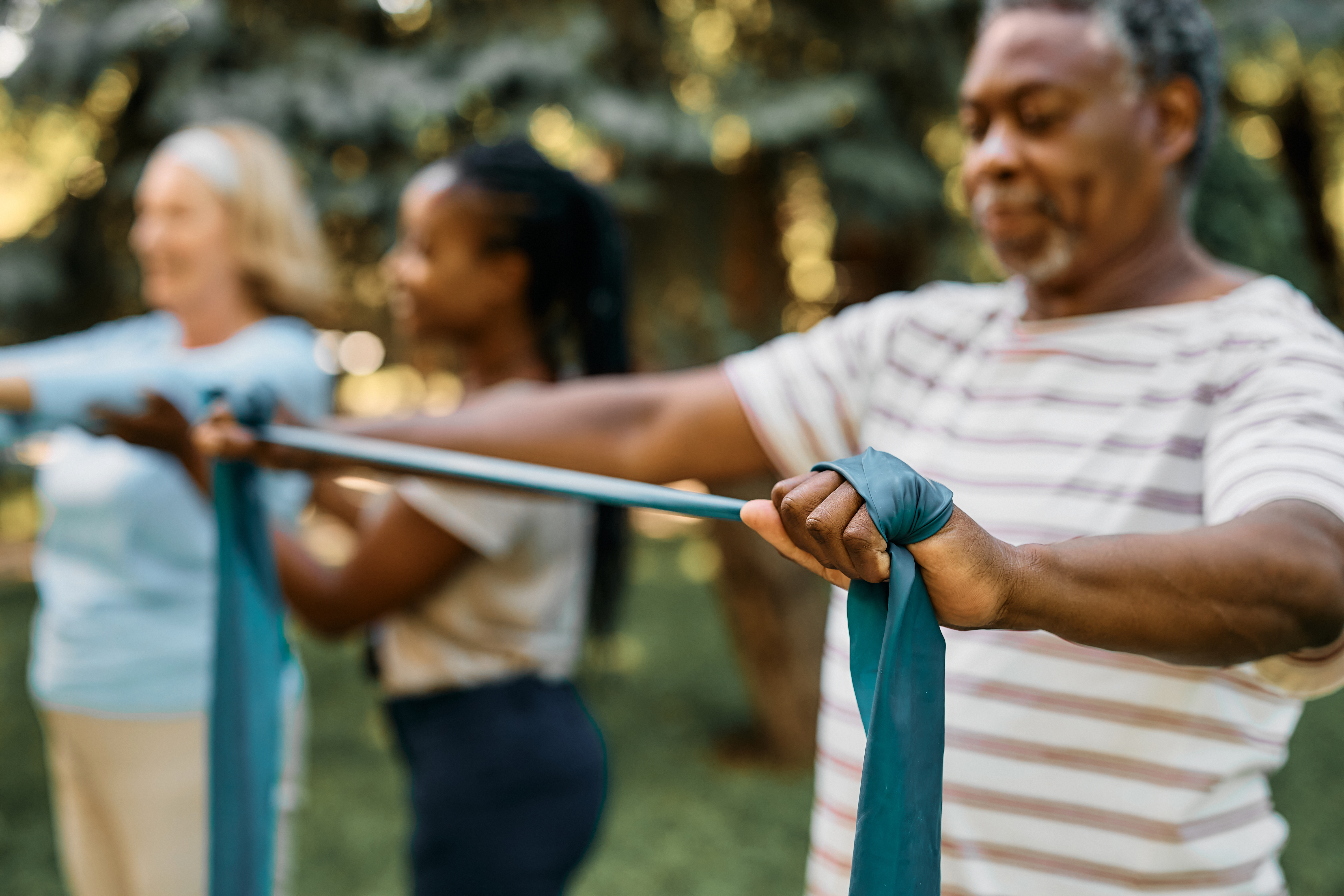 People exercising outdoors using long resistance bands, stretching them out in front of their bodies.