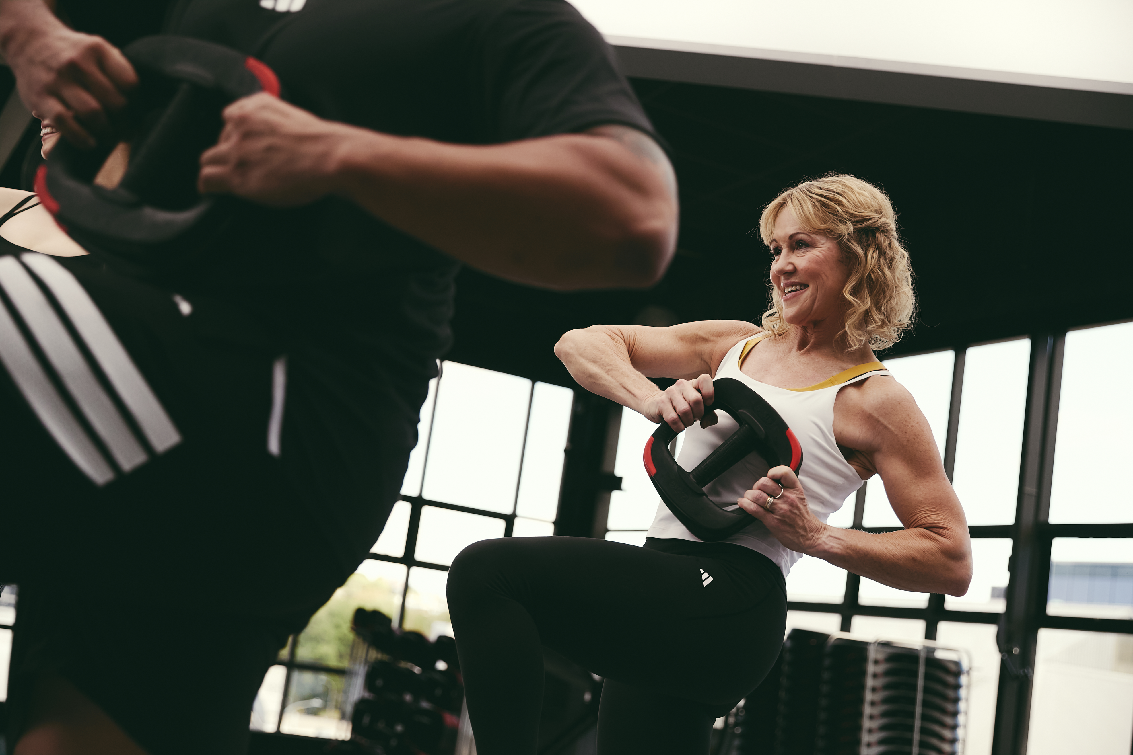People taking part in a core strength class, lifting weight plates while balancing on one leg inside a gym studio.