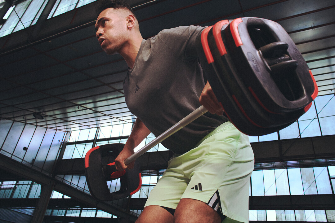 A person lifting a barbell loaded with large weight plates inside a spacious gym with high windows.