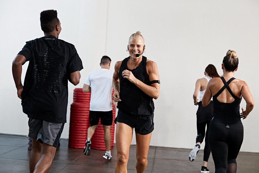 People running and exercising together in a group fitness class inside a gym studio.