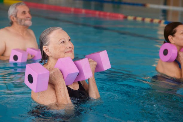 People taking part in an aqua exercise class, lifting pink foam dumbbells while standing in a swimming pool.