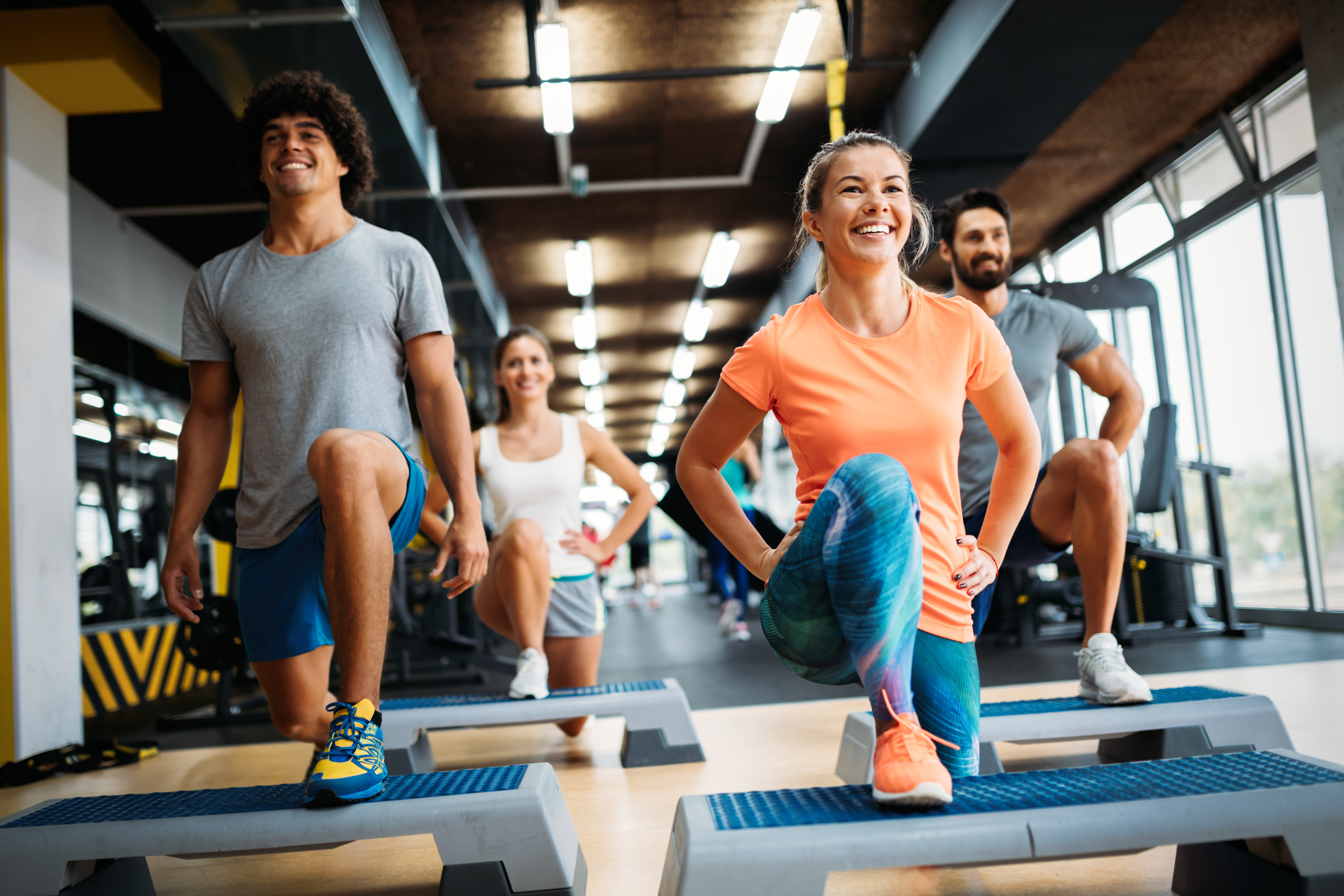 Group fitness class in a gym with participants performing step exercises on platforms