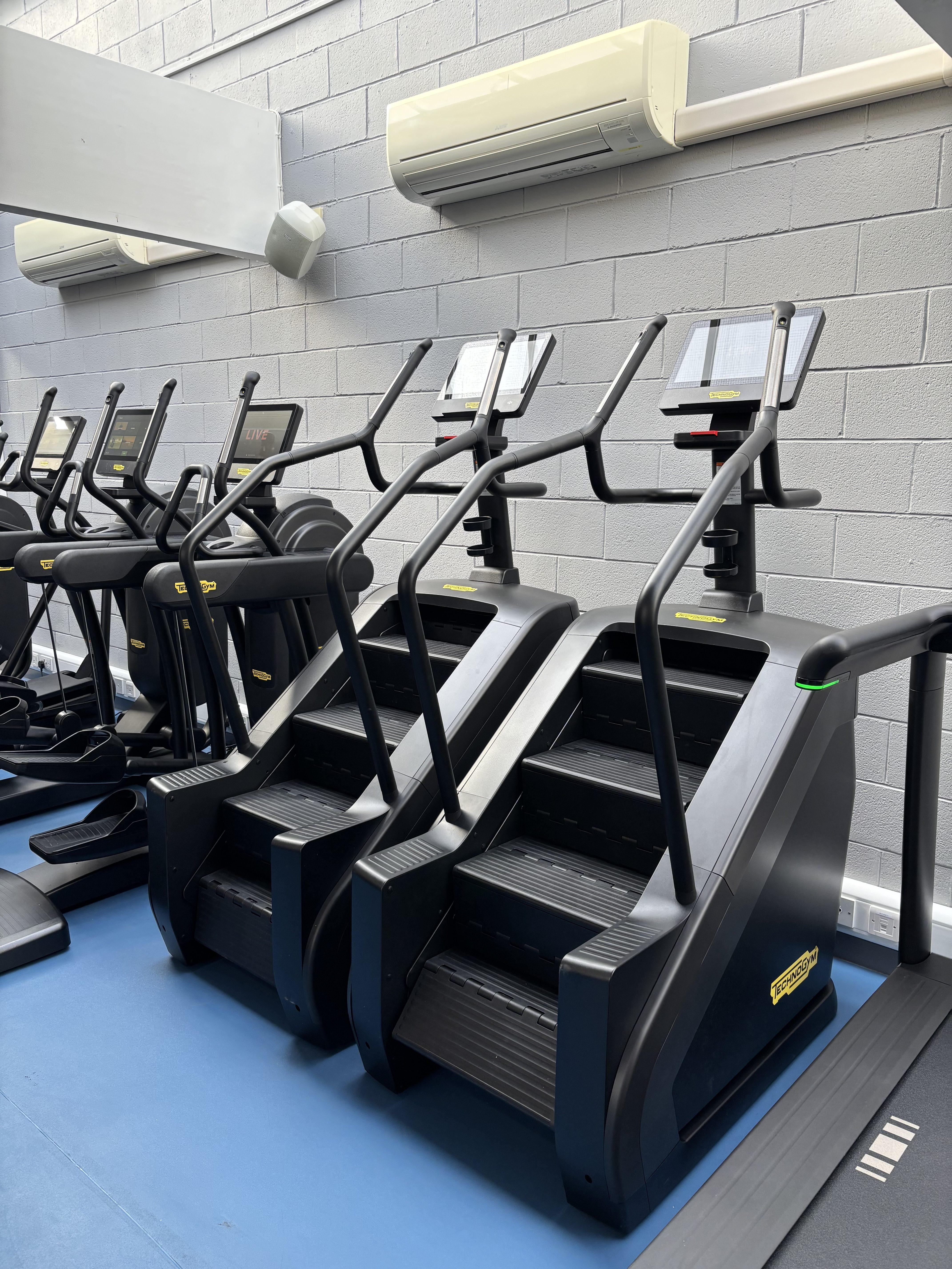 Row of stair-climbing machines lined up against a blue wall in a gym.