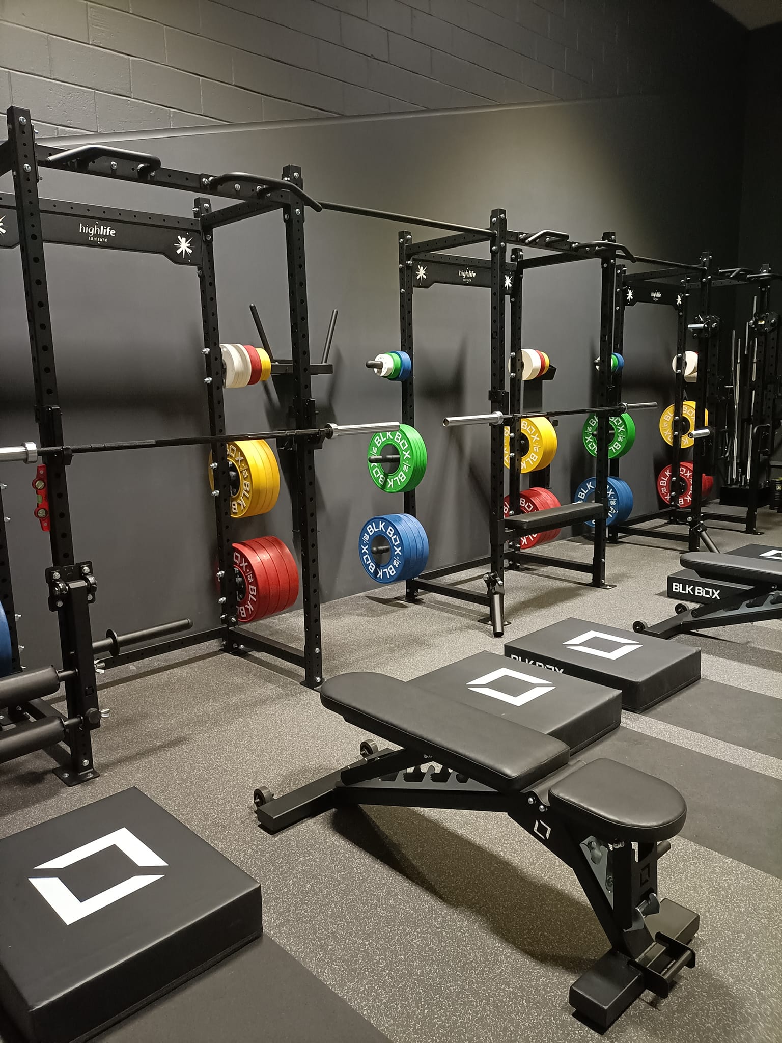 Close-up of weightlifting equipment with barbells and colored plates against dark walls.
