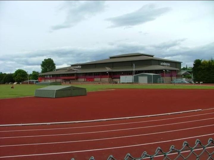 An outdoor running track with a sports building in the background under a cloudy sky.