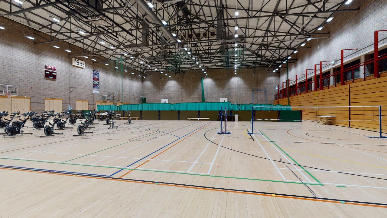 A wide view of a sports hall showing both exercise bikes and badminton courts on the wooden floor.